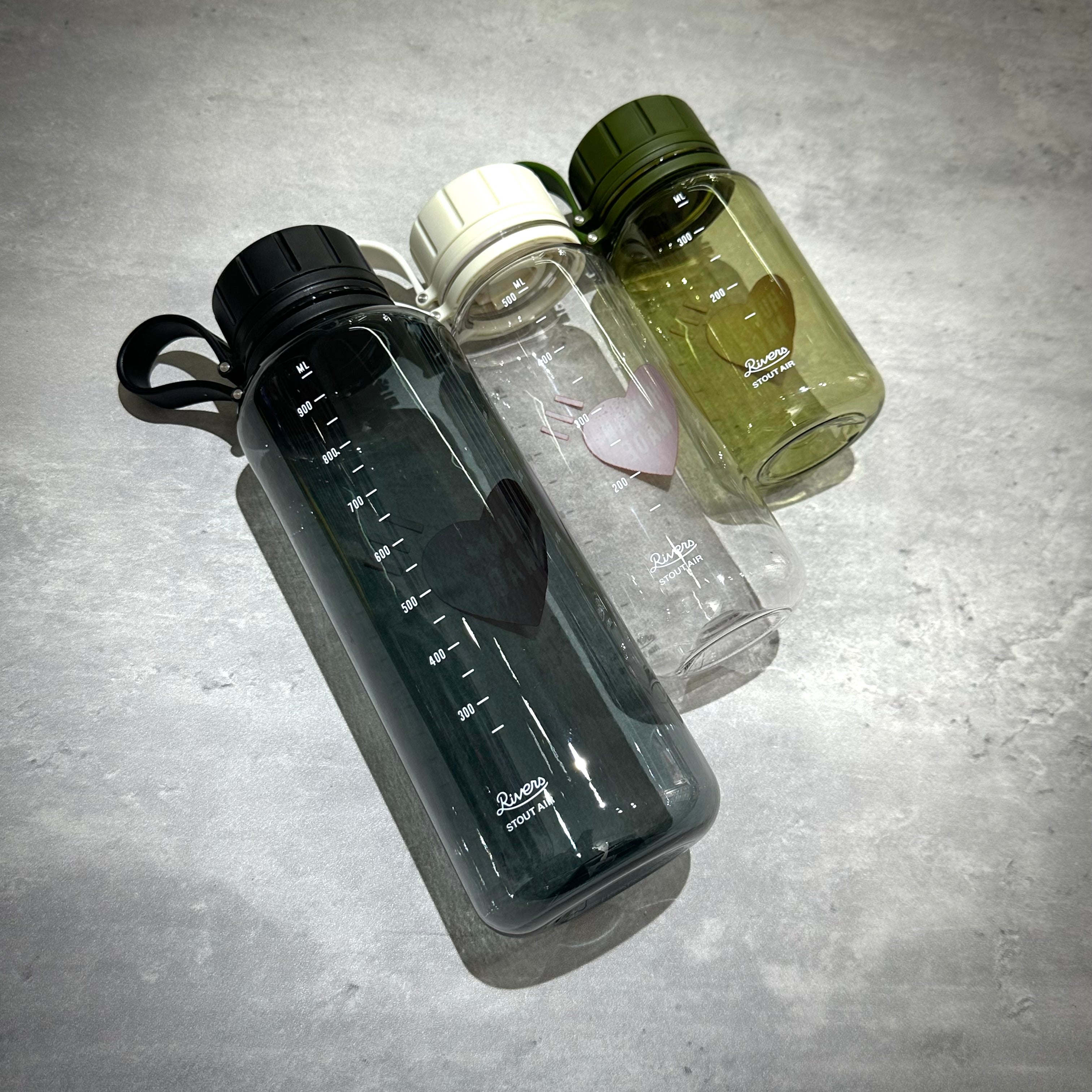 Human Made Water Bottle in three colors: black, clear, and green, showcasing heart design and measurement markings.