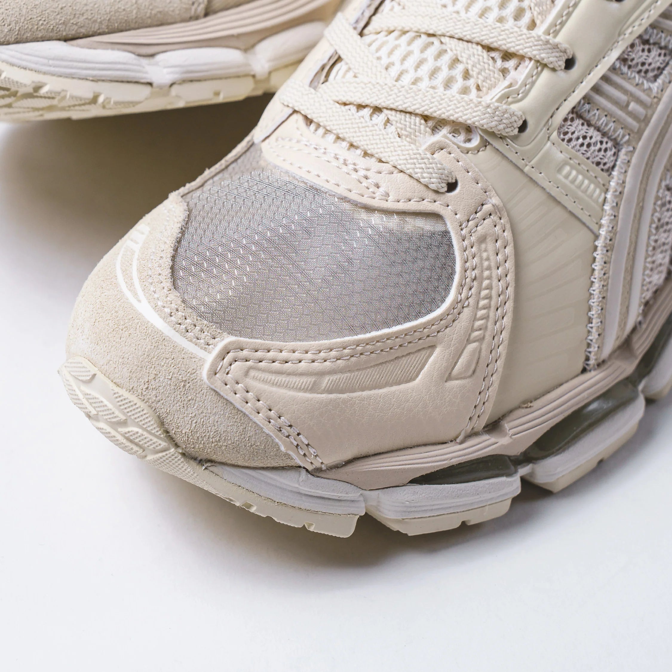Close-up view of the Madness x Invincible x Asics Gel-Kayano 12.1 Vanilla sneaker detailing the cream upper and mesh design.