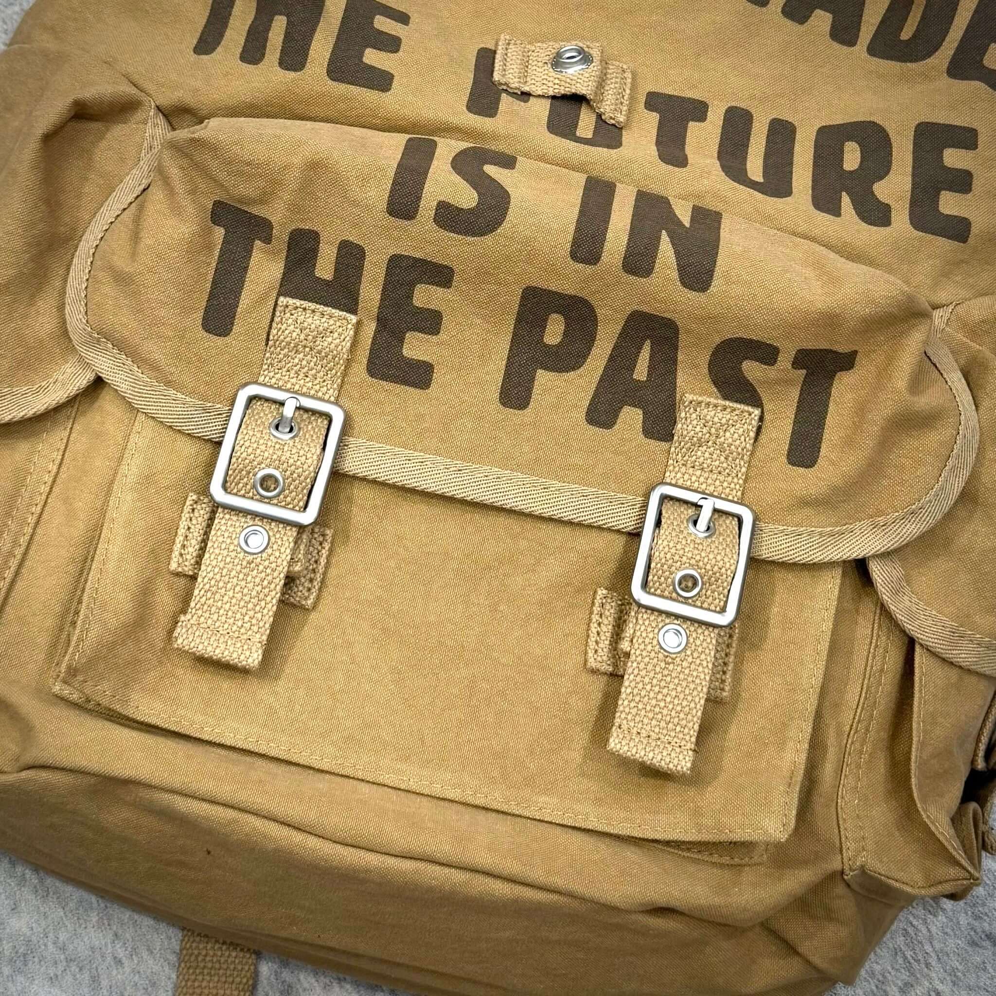 Close-up of the Human Made Hunting Backpack showing the flap and straps with text that reads 'THE FUTURE IS IN THE PAST'.