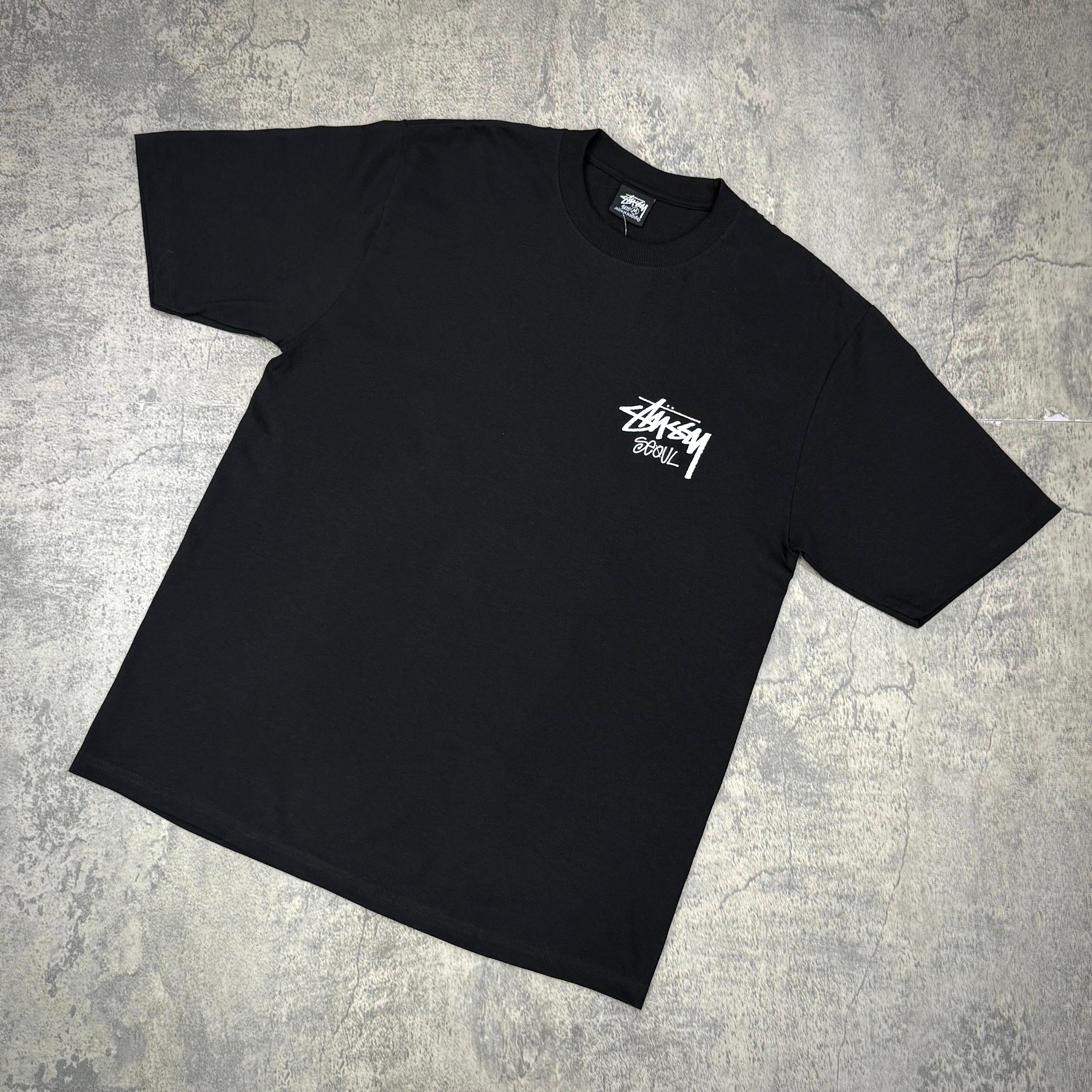 Black Stussy Seoul Exclusive Logo Tee displayed on a gray background, showcasing front logo design.