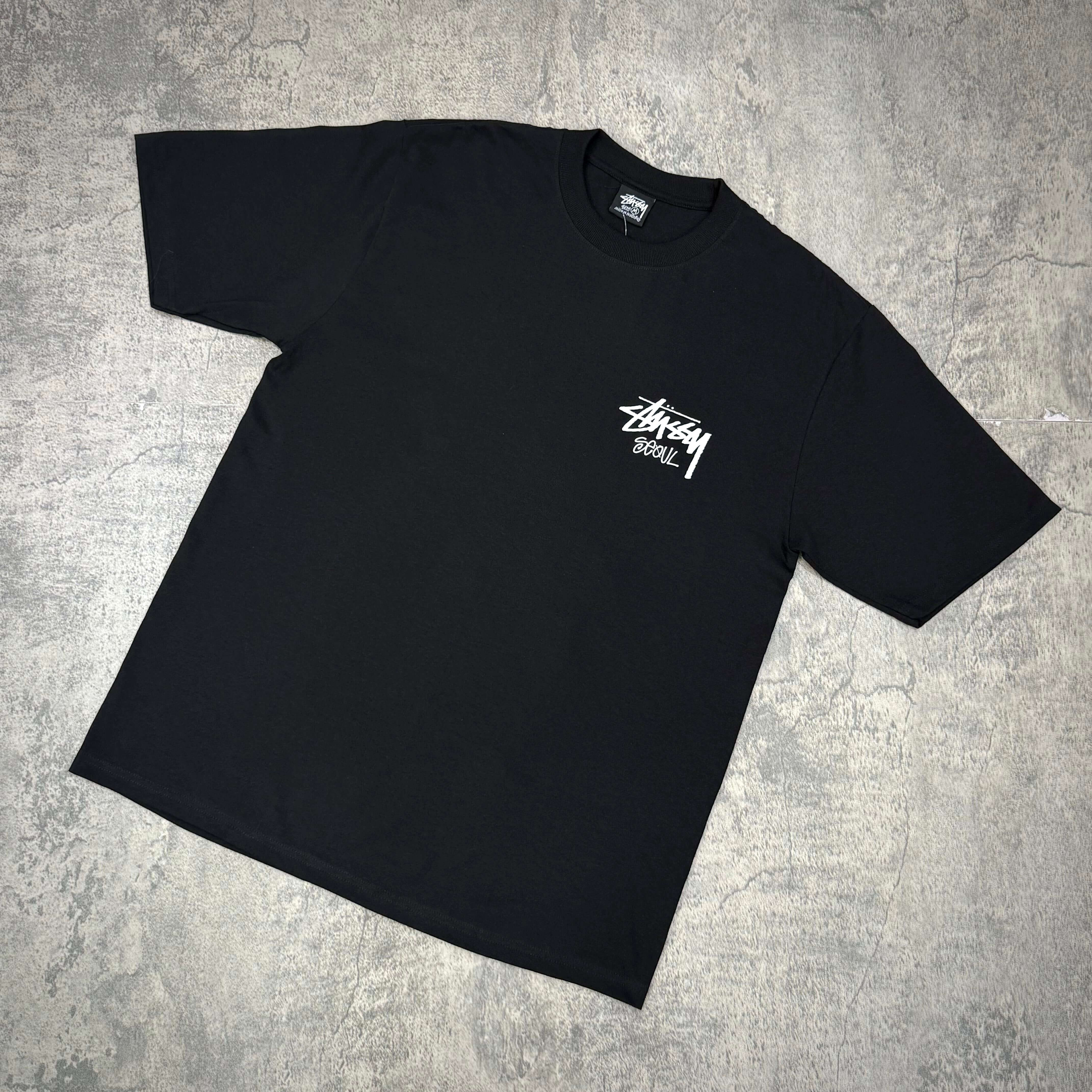 Black Stussy Seoul Exclusive Logo Tee displayed on a gray background, showcasing front logo design.