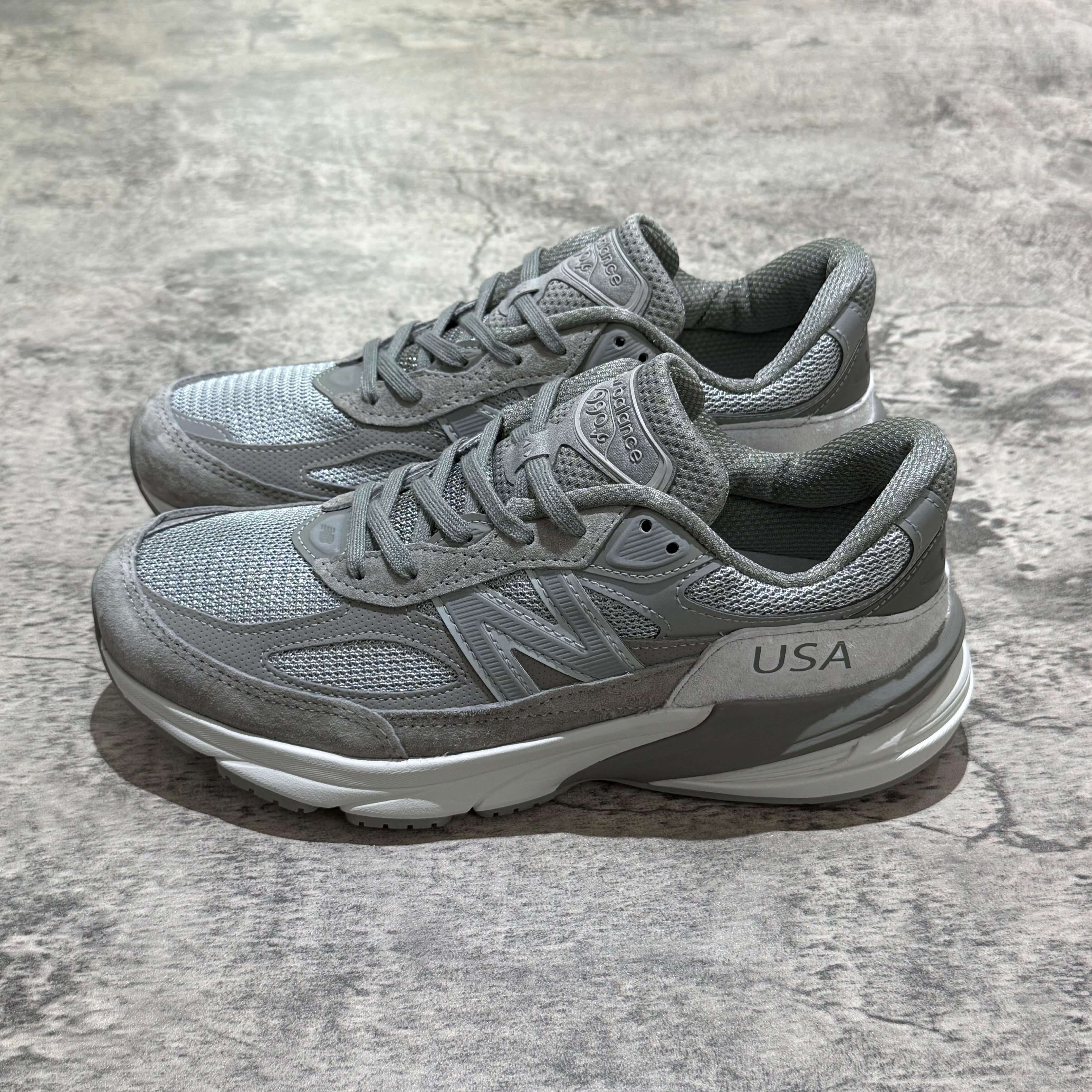 New Balance x Wtaps 990v6 in grey colorway displayed on a textured surface.