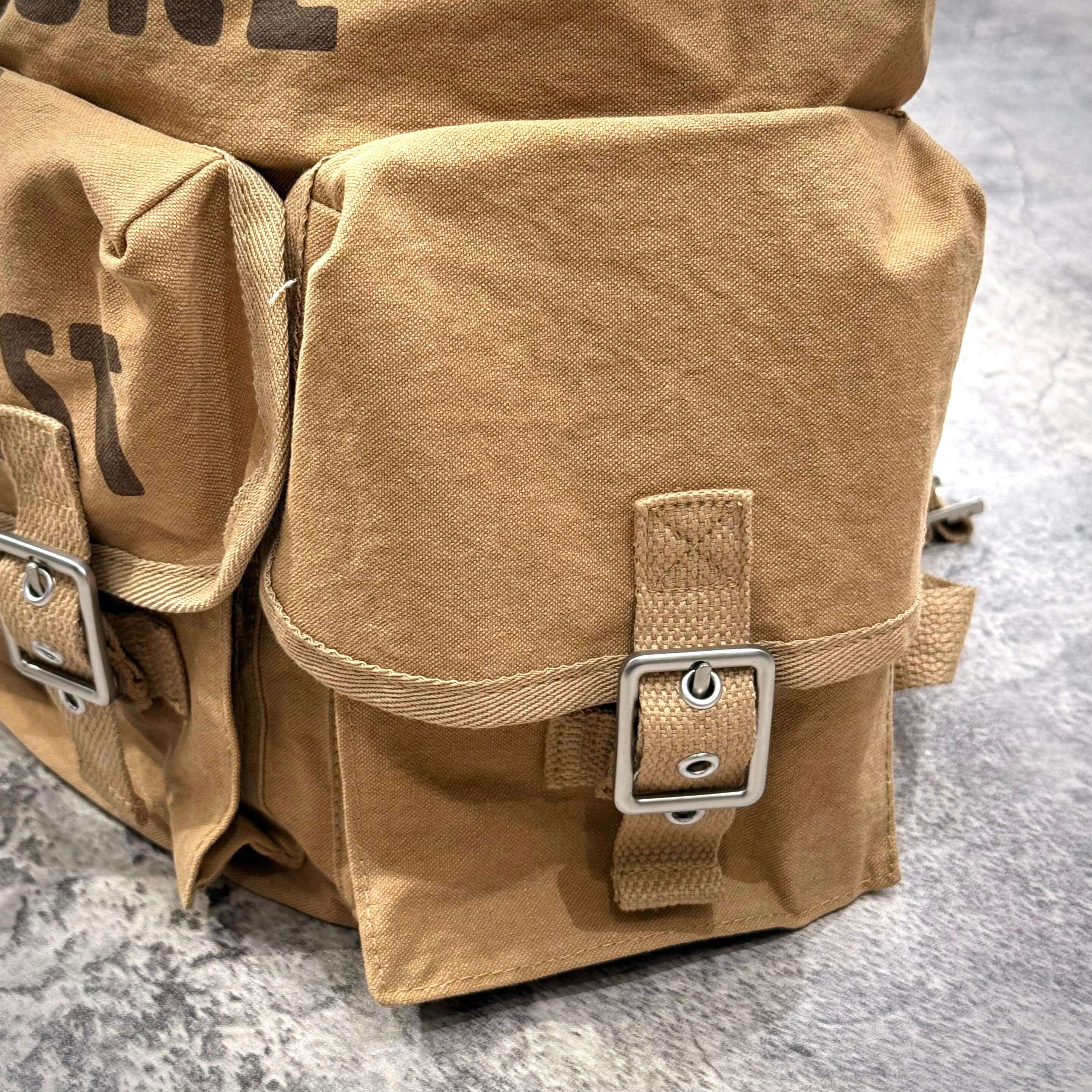 Close-up of the Human Made Hunting Backpack showing pockets and buckles on a textured surface.