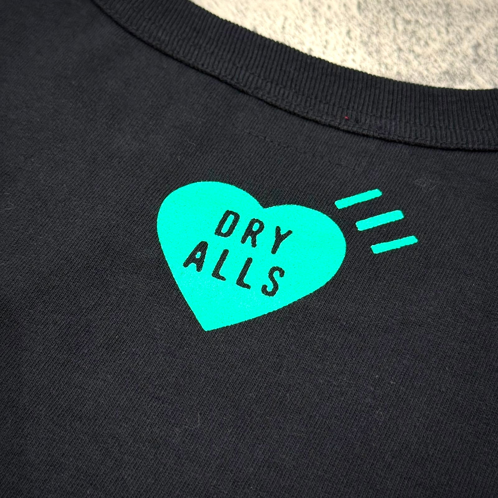 黑色T恤胸前圖案顯示綠色心形標誌,內有'DRY ALLS'字樣,時尚設計