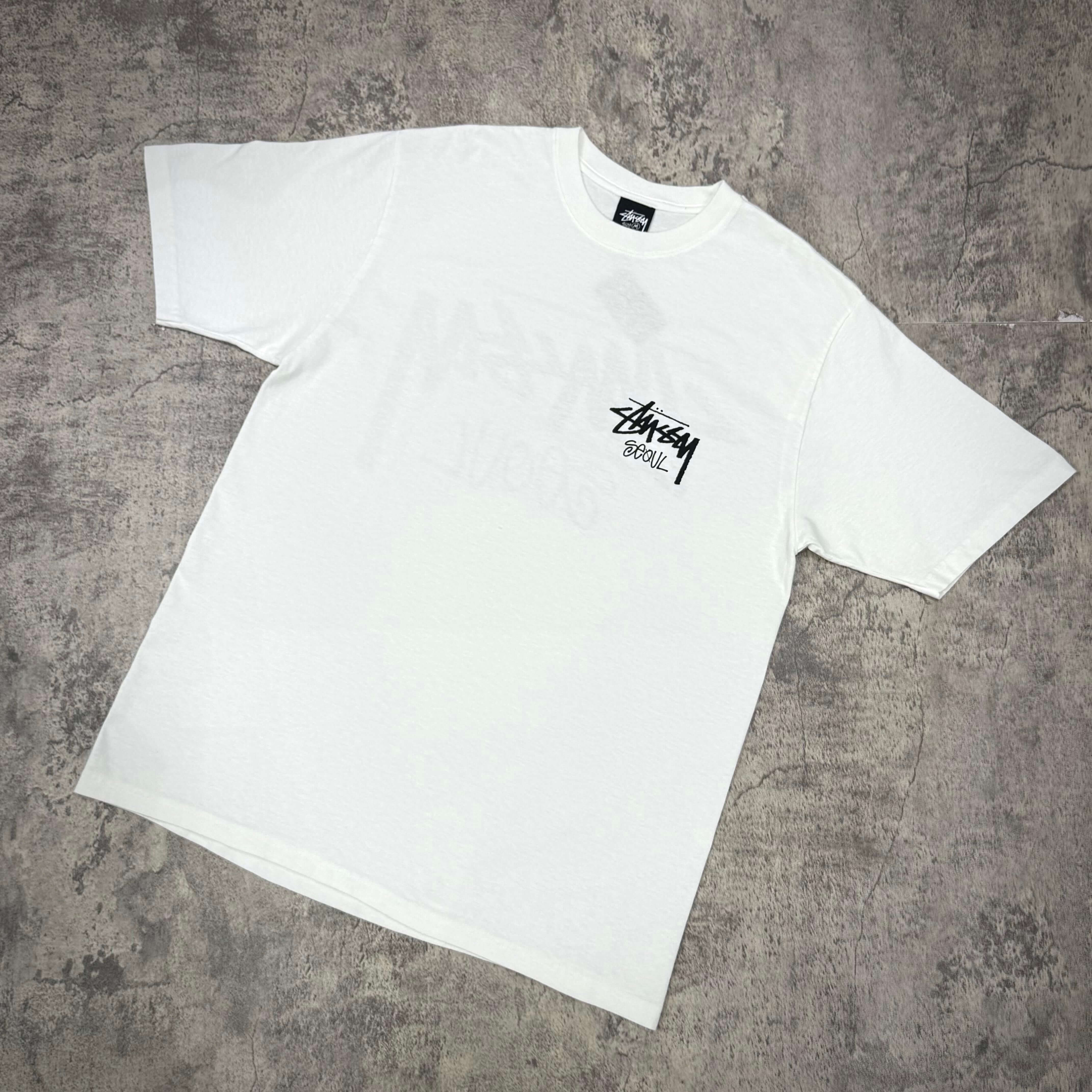 Stussy Seoul Exclusive Logo Tee - Black / White displayed on a gray background