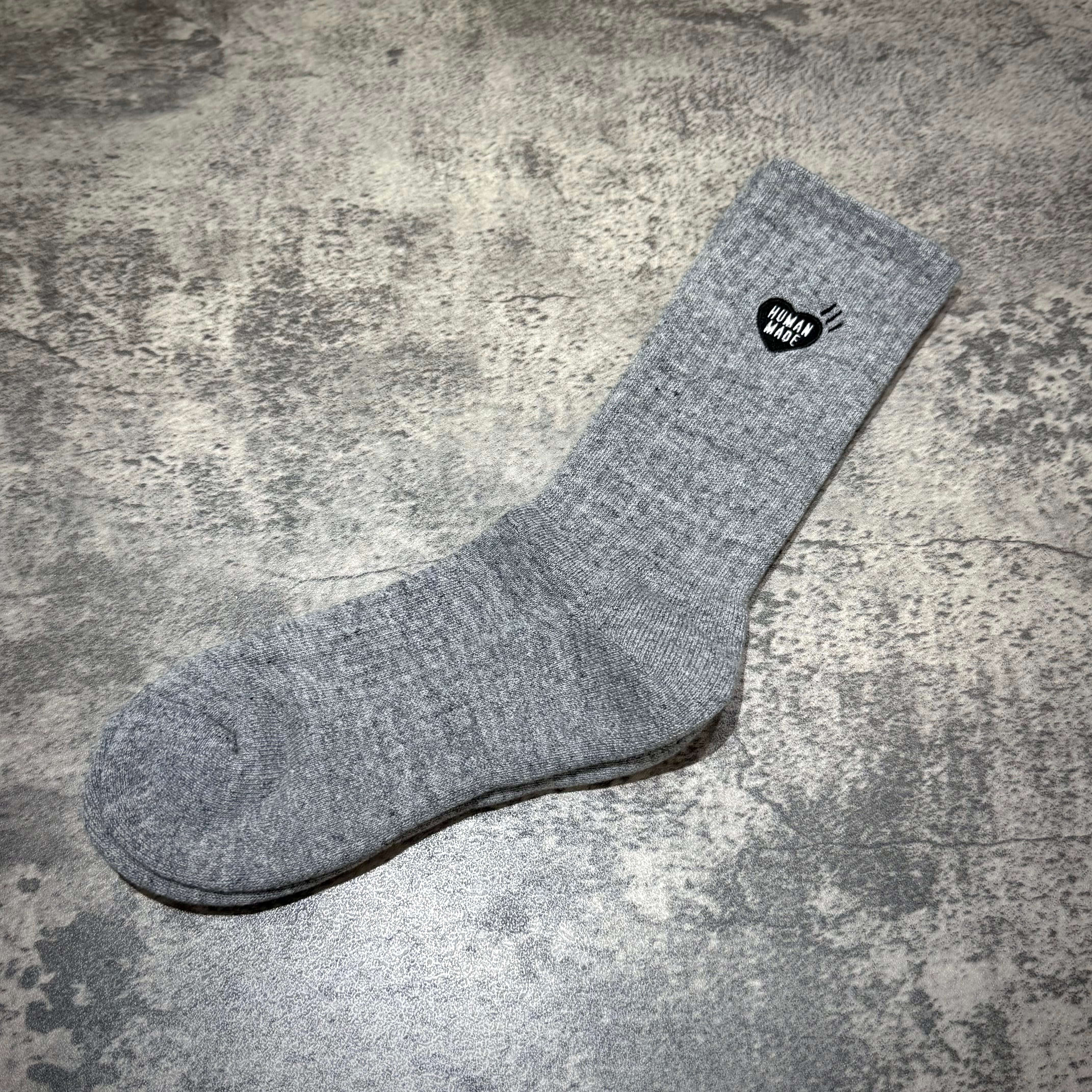 Human Made Pile Socks displayed on a textured surface, showcasing their unique design and logo.