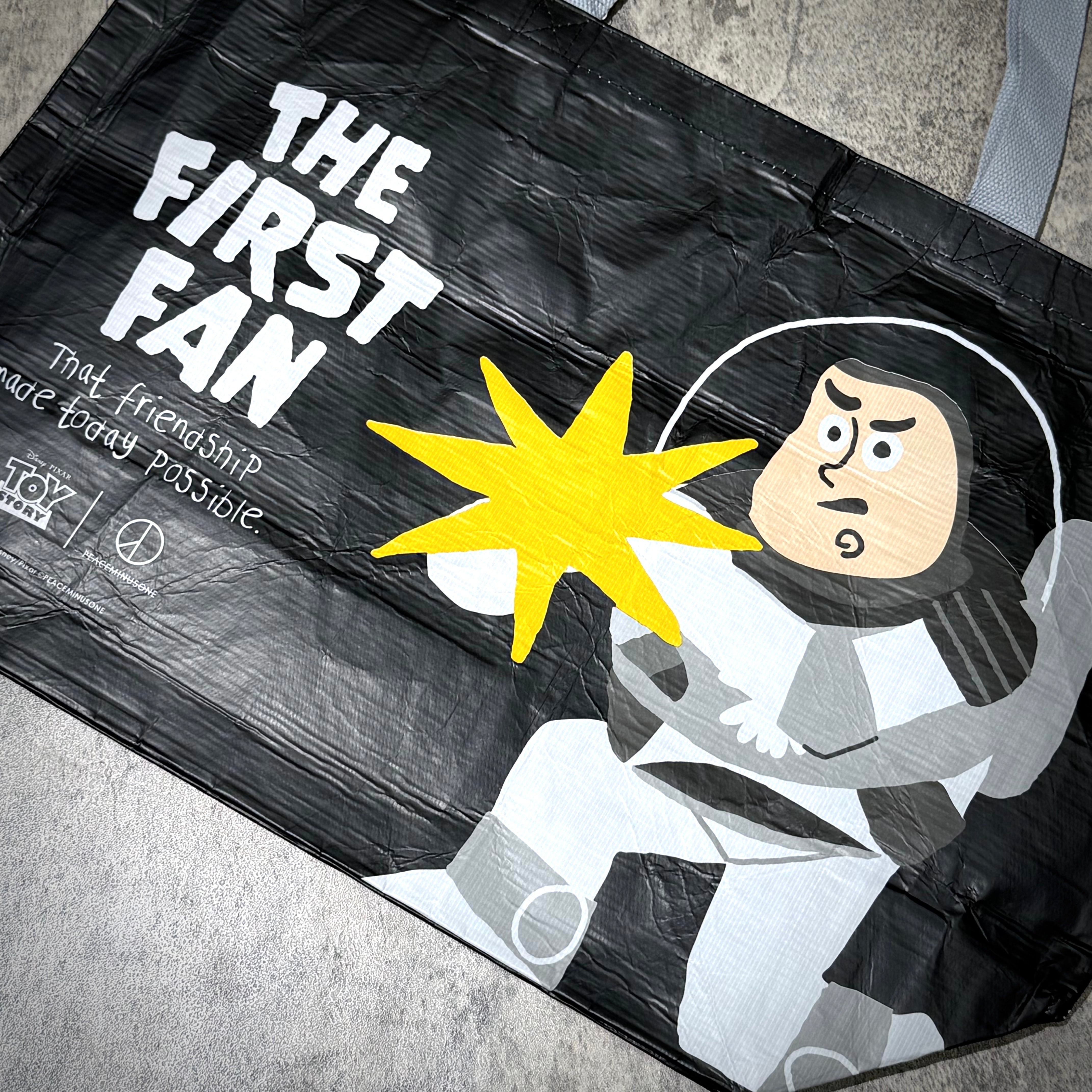 PEACEMINUSONE x Toy Story reusable bag featuring Buzz Lightyear with text "THE FIRST FAN" and bright energy burst design.