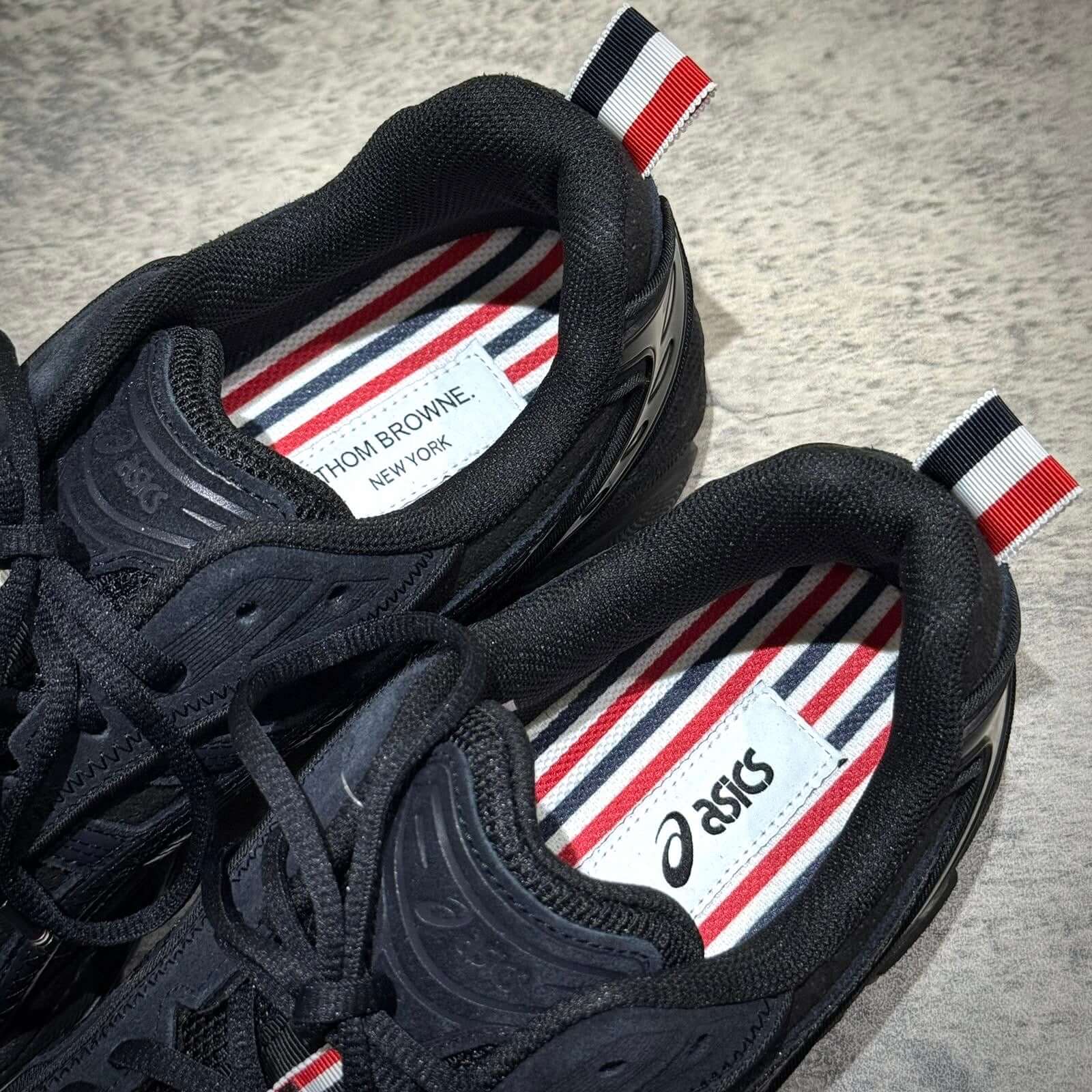 Top view of Thom Browne x Asics Gel-Kayano 14 in black with striped insoles and branding labels.
