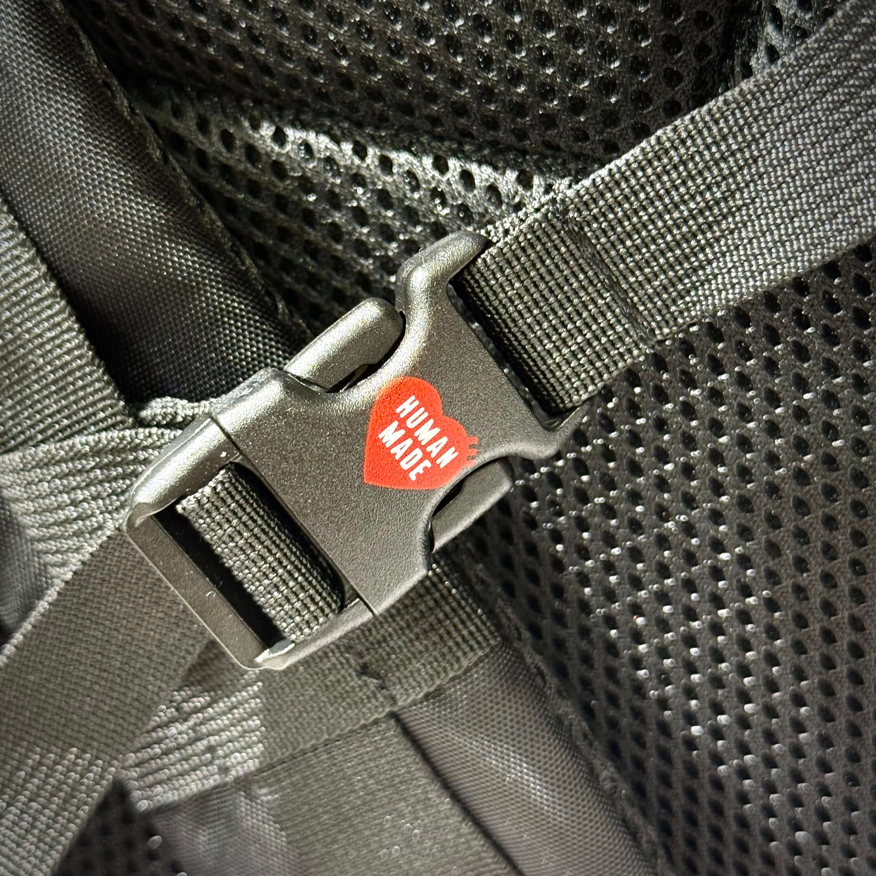 Close-up of Human Made Military Backpack buckle detail showcasing the brand's iconic logo.