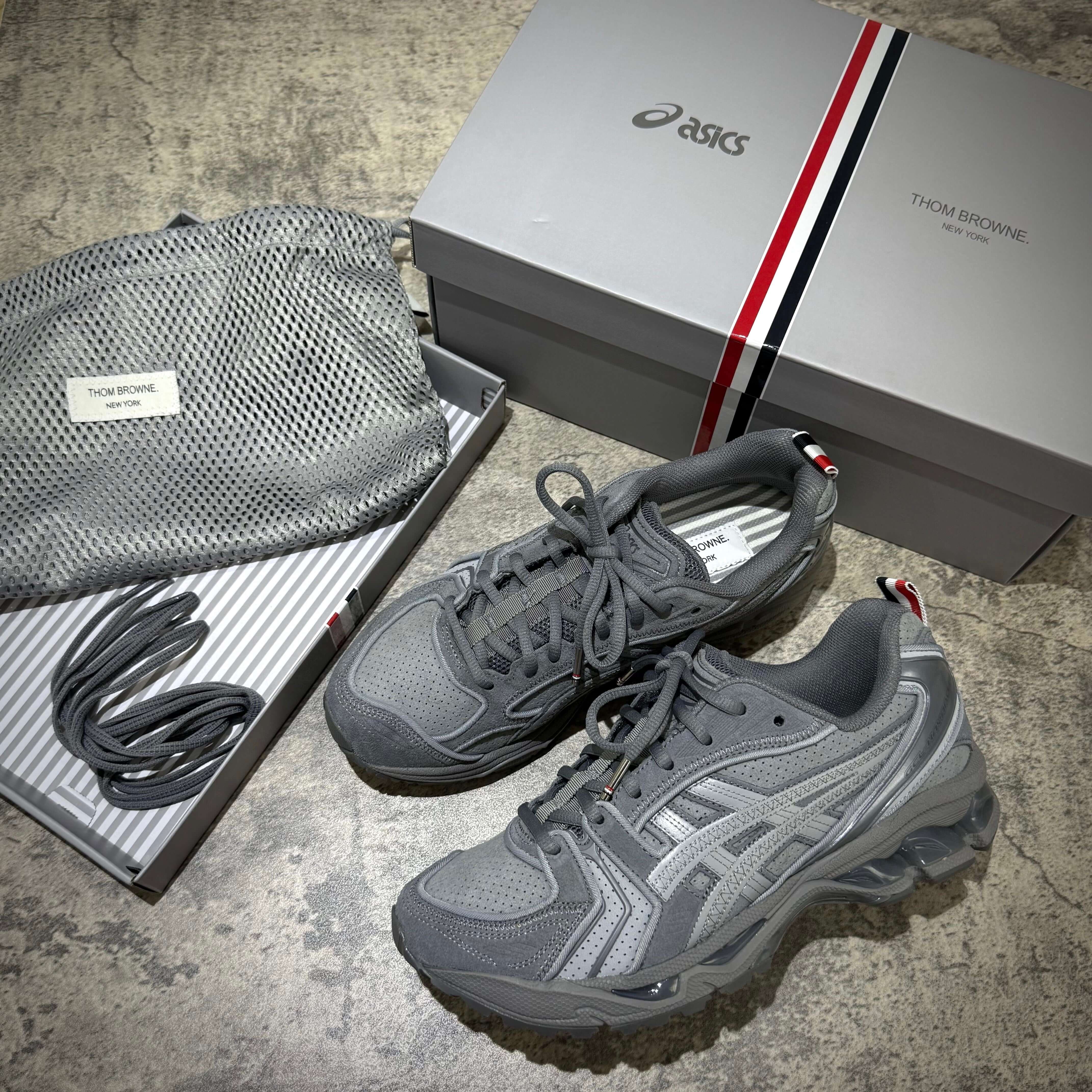 Thom Browne x Asics Gel-Kayano 14 in Grey with packaging and accessories displayed.