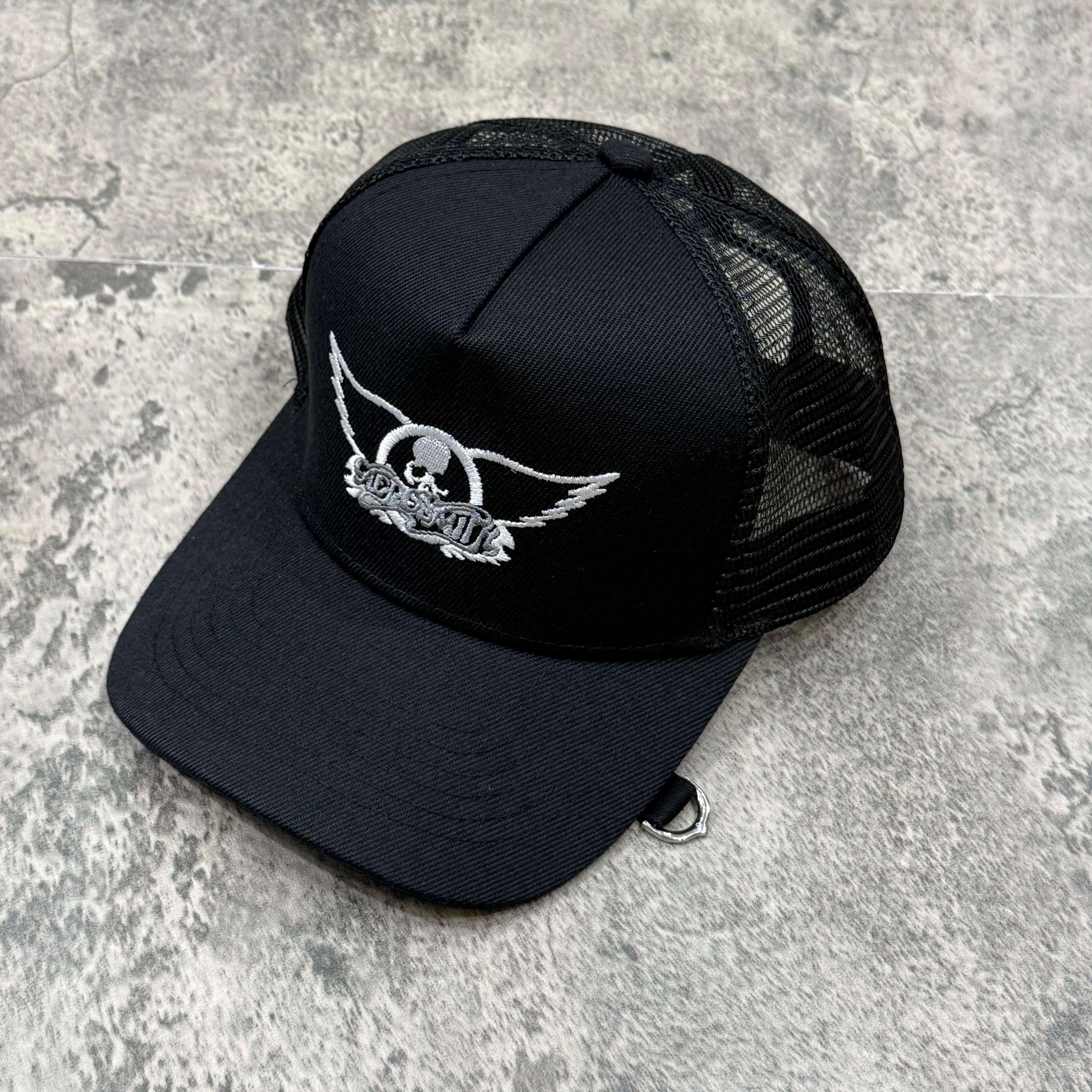 Aerosmith x Mastermind World Wing And Skull Logo Cap displayed on a textured surface.