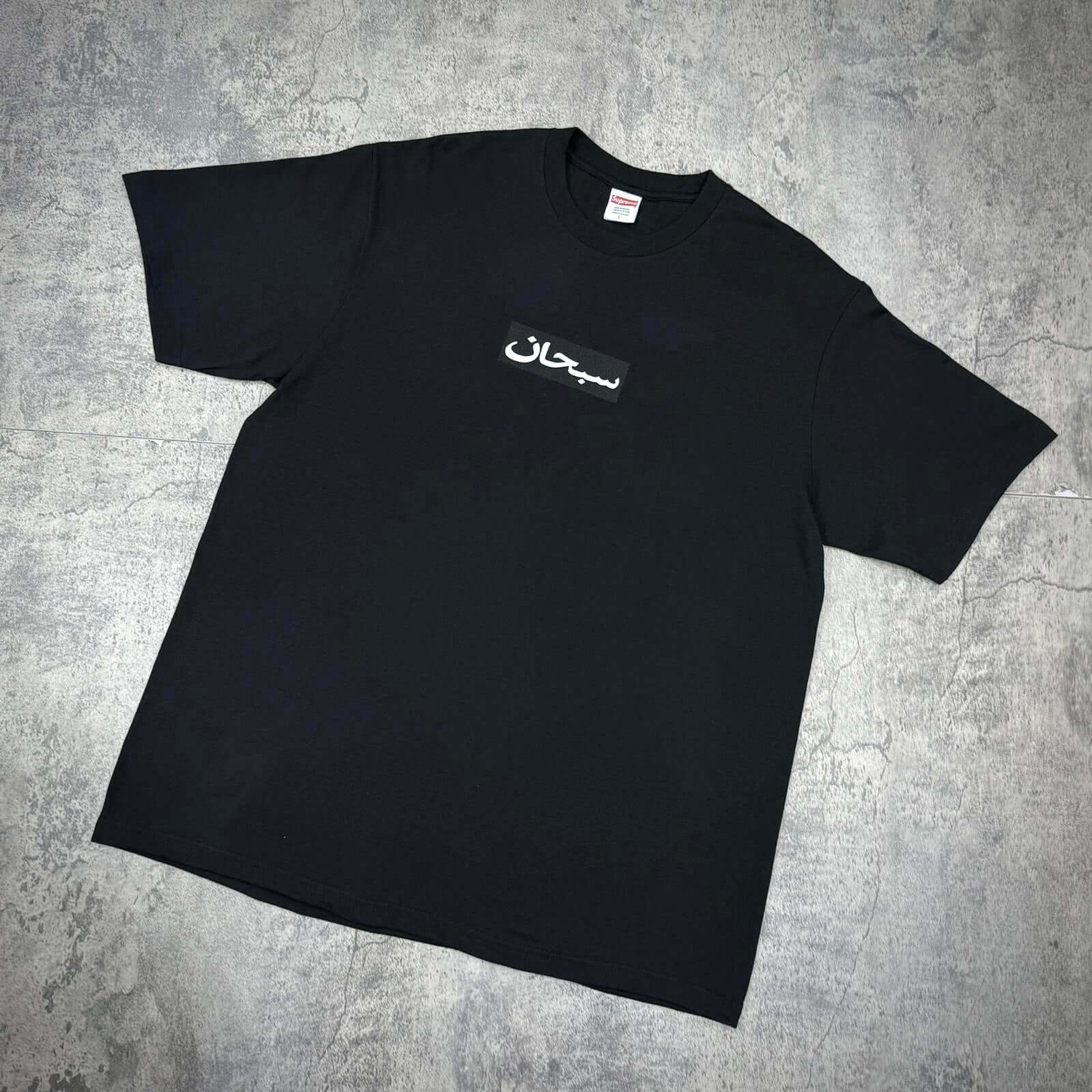 Supreme Arabic Box Logo Tee displayed on a gray surface, featuring a black t-shirt with Arabic logo.