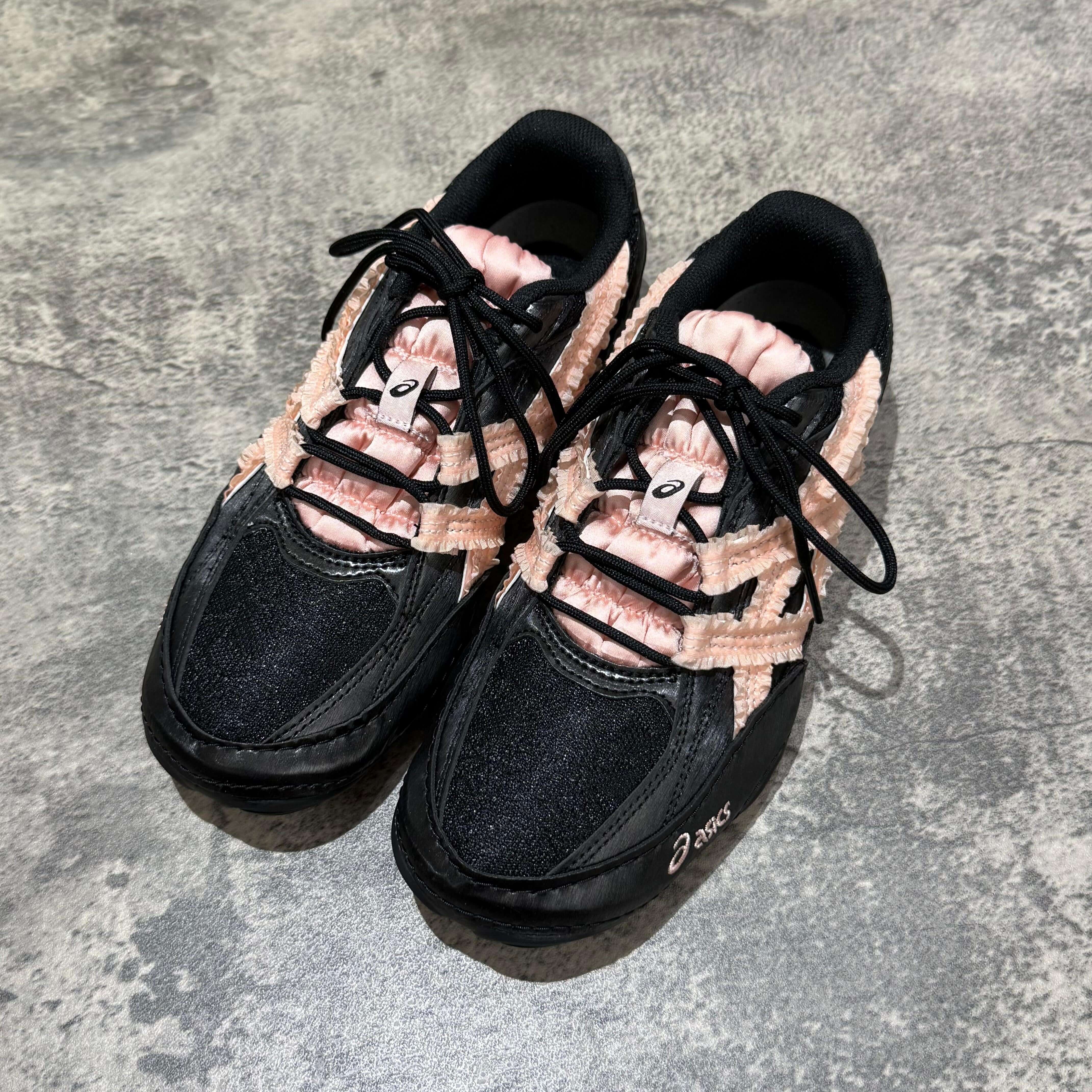 Asics x Empty Behavior Hypersync shoes in black and pink colorway on a textured surface.