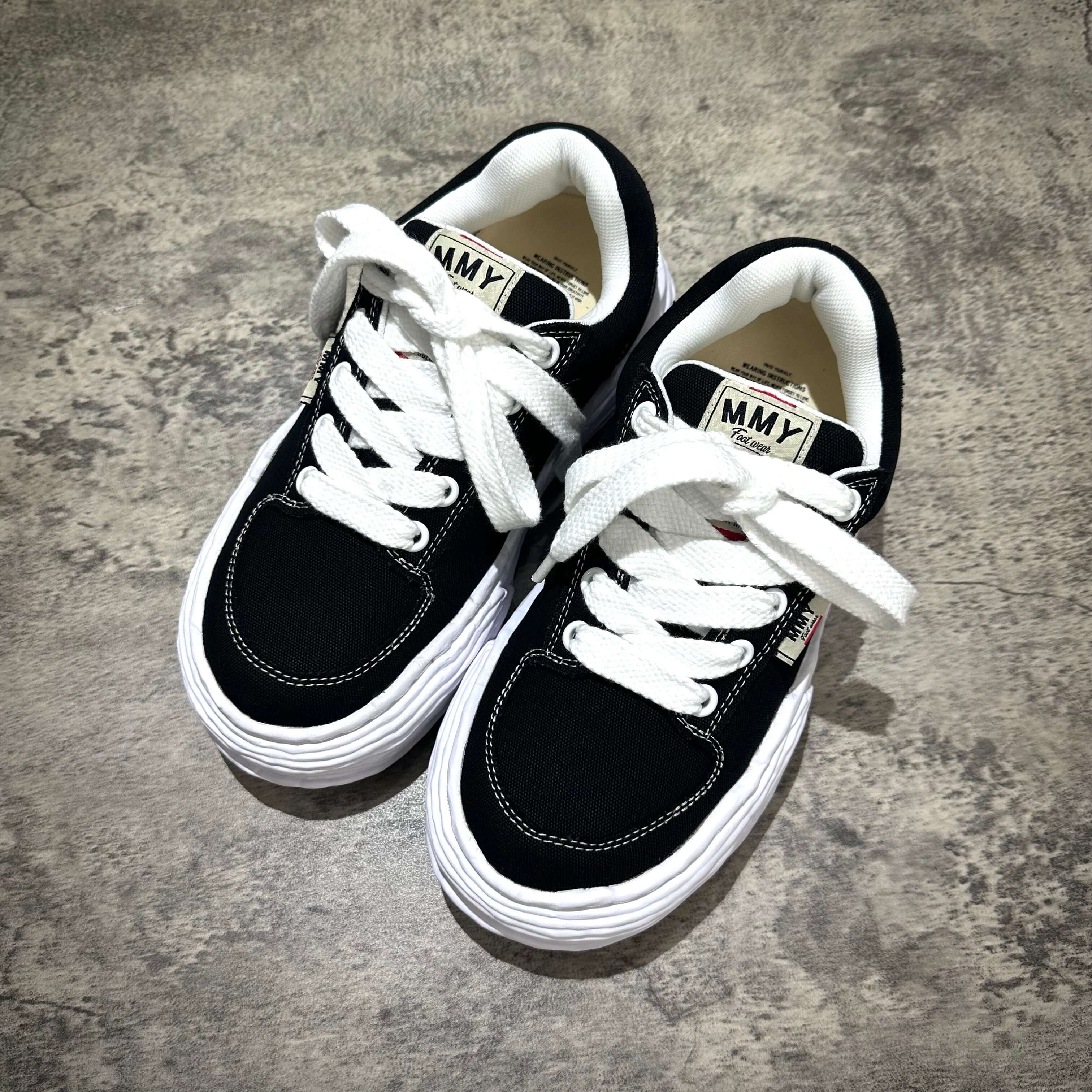 MMY Oliver Canvas Low - Black sneakers with white laces on a gray background.