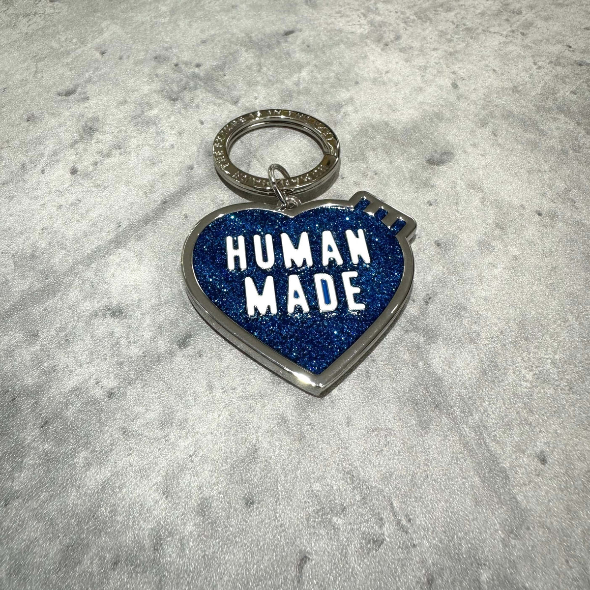 Human Made Store Exclusive Heart Keychain with blue glitter finish and keyring, showcasing bold text 'HUMAN MADE'.