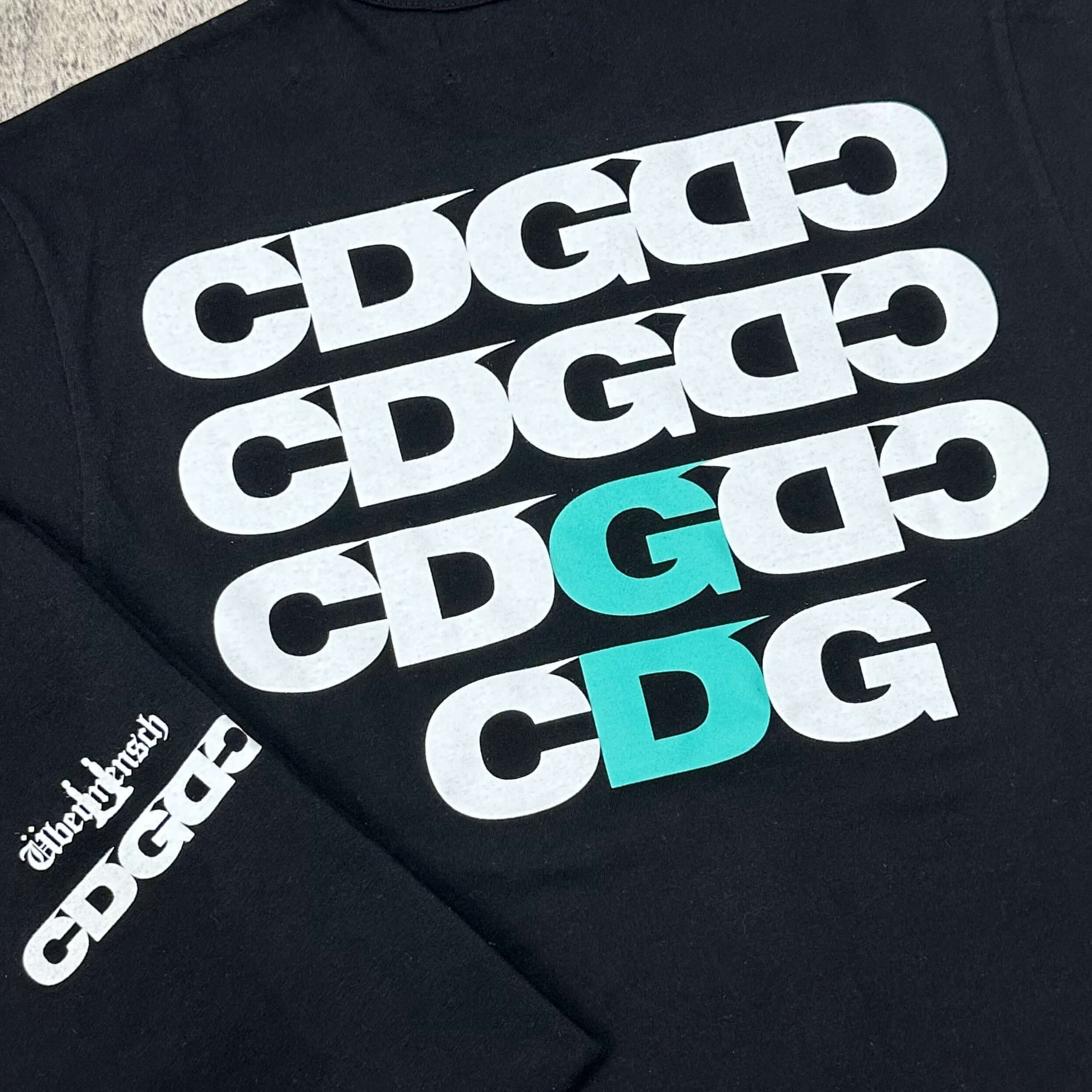 CDG x G-DRAGON Ubermensch Symbol Tee featuring bold CDG logos on a black background.