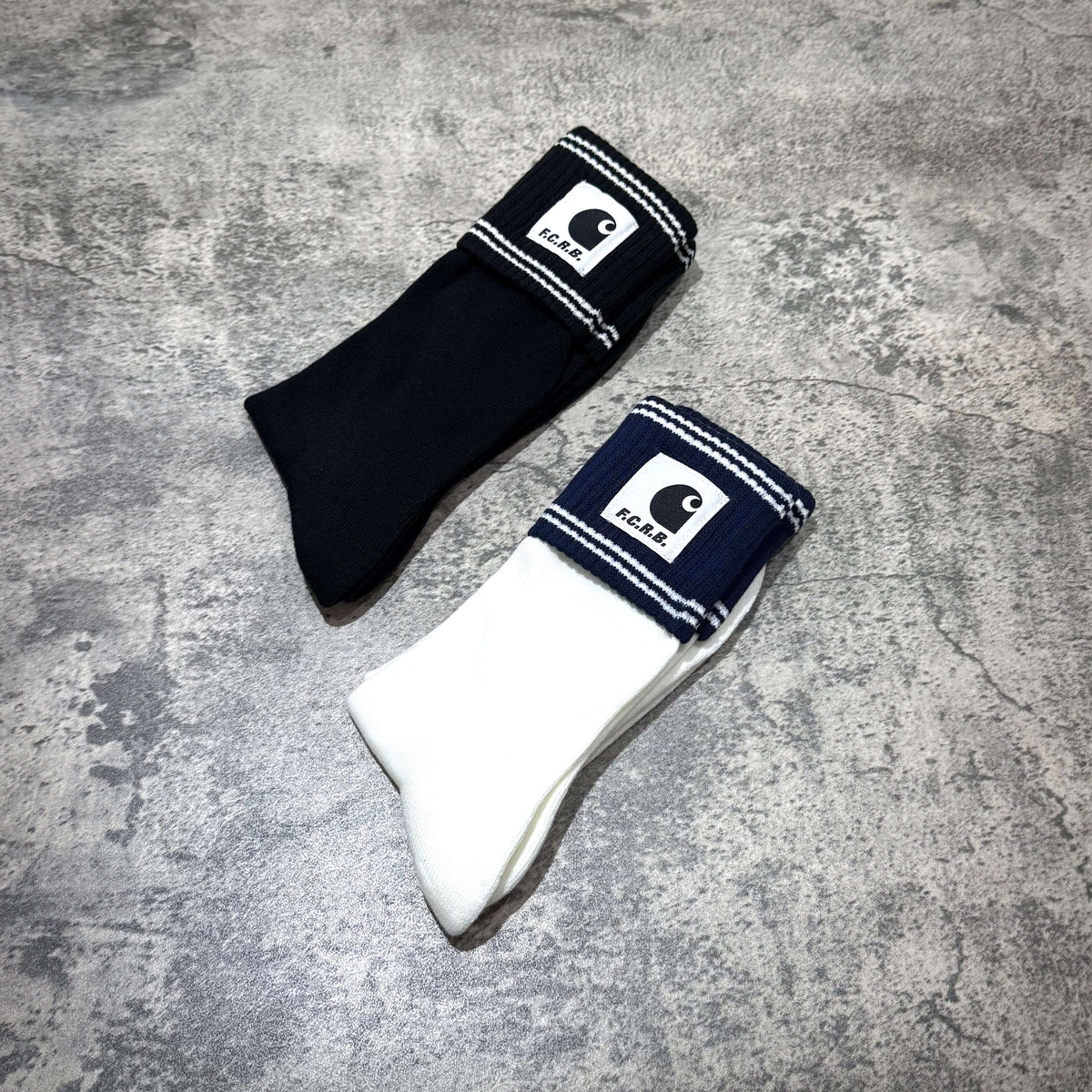 Carhartt WIP x F.C.Real Bristol Cuff Socks in black and white on a textured surface.