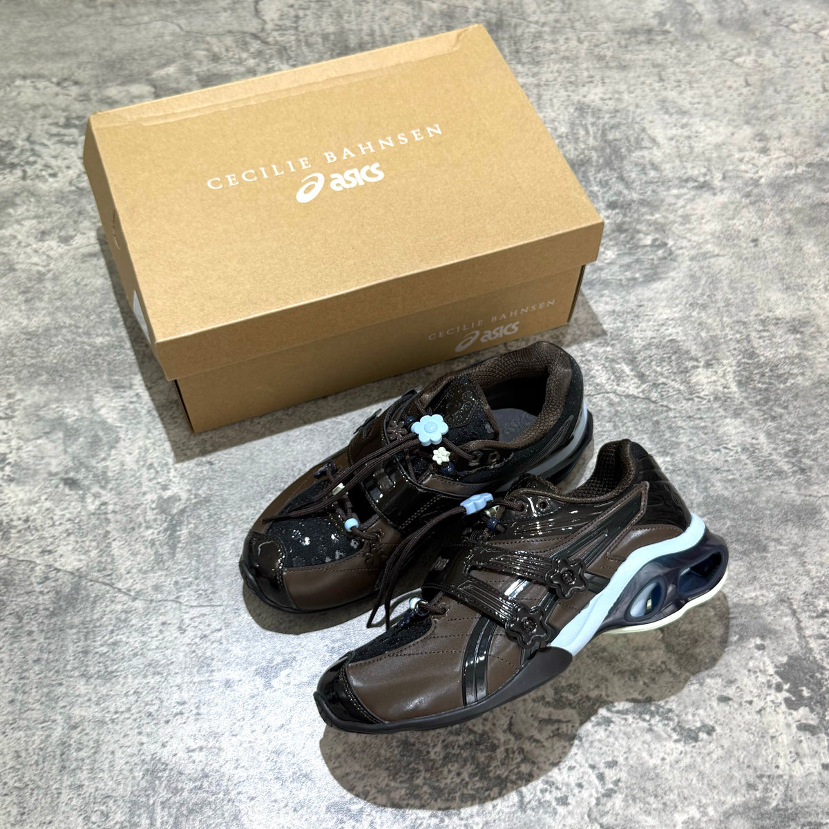 Cecilie Bahnsen x Asics Gel-Kinetic FR - Black Coffee 1203B171-001 shoes with packaging on a textured surface.