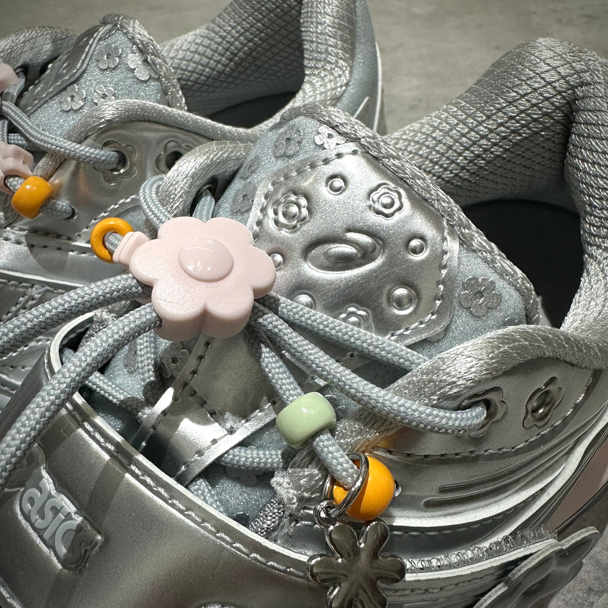Close-up of Cecilie Bahnsen x Asics Gel-Kinetic FR - Pure Silver shoe detailing with floral charms and lace design.