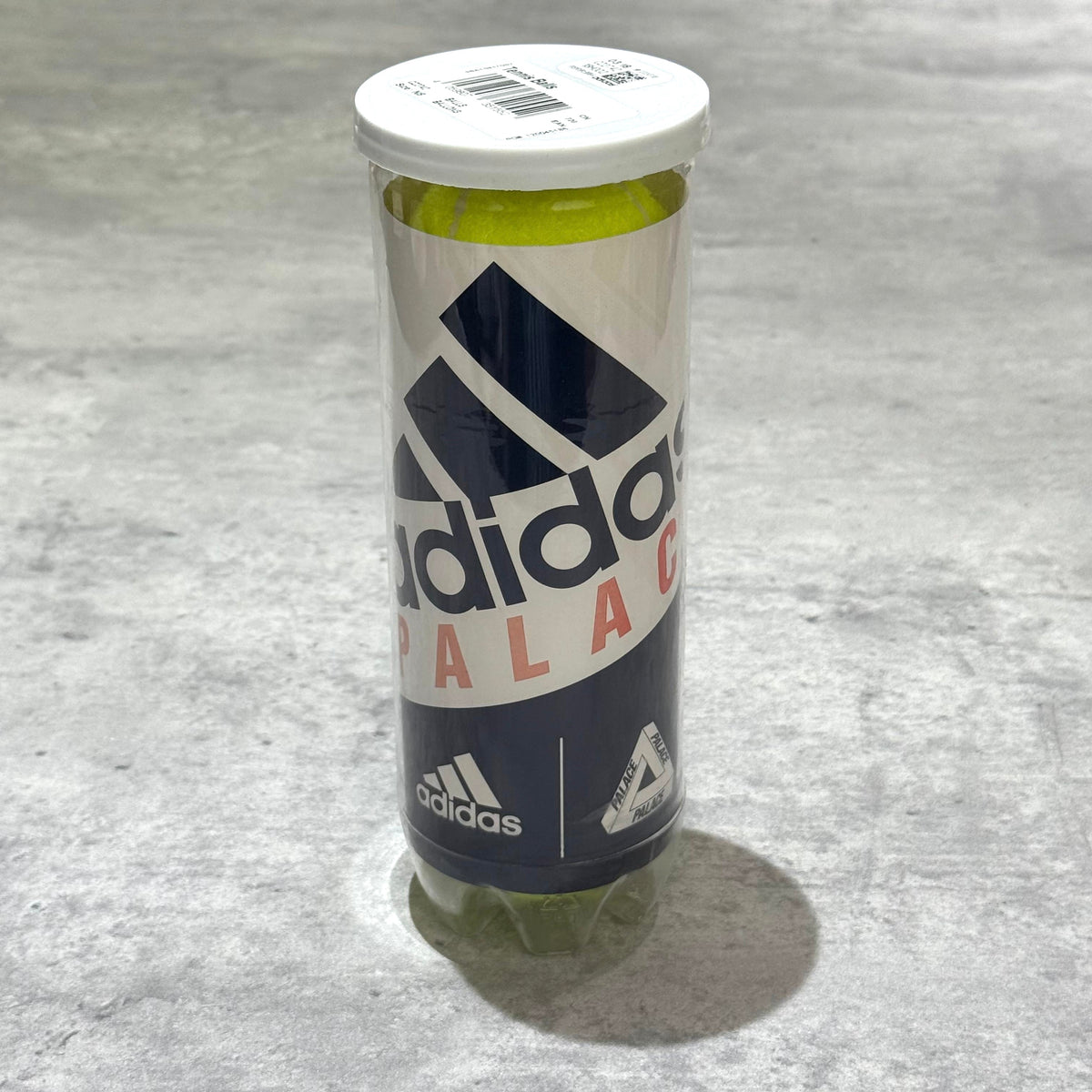 Palace x adidas Tennis Balls in a clear container showcasing the branding on a textured surface.