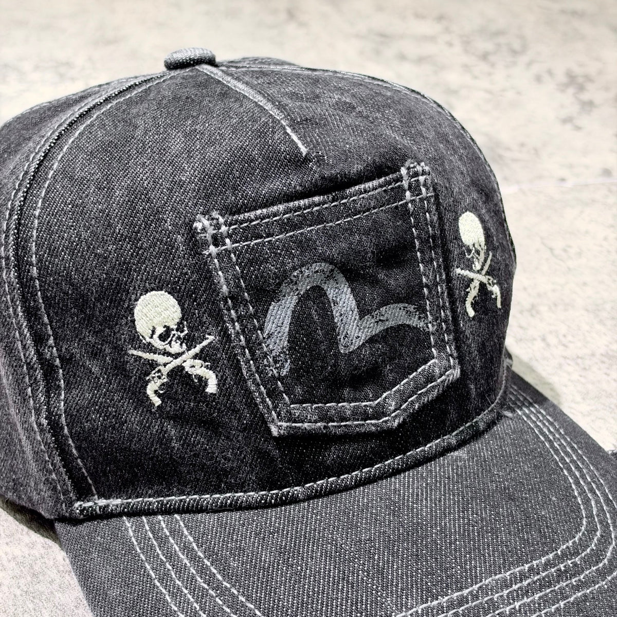 Close-up of Evisu x Mastermind Japan x Roarguns Cap featuring skull motifs and denim texture.