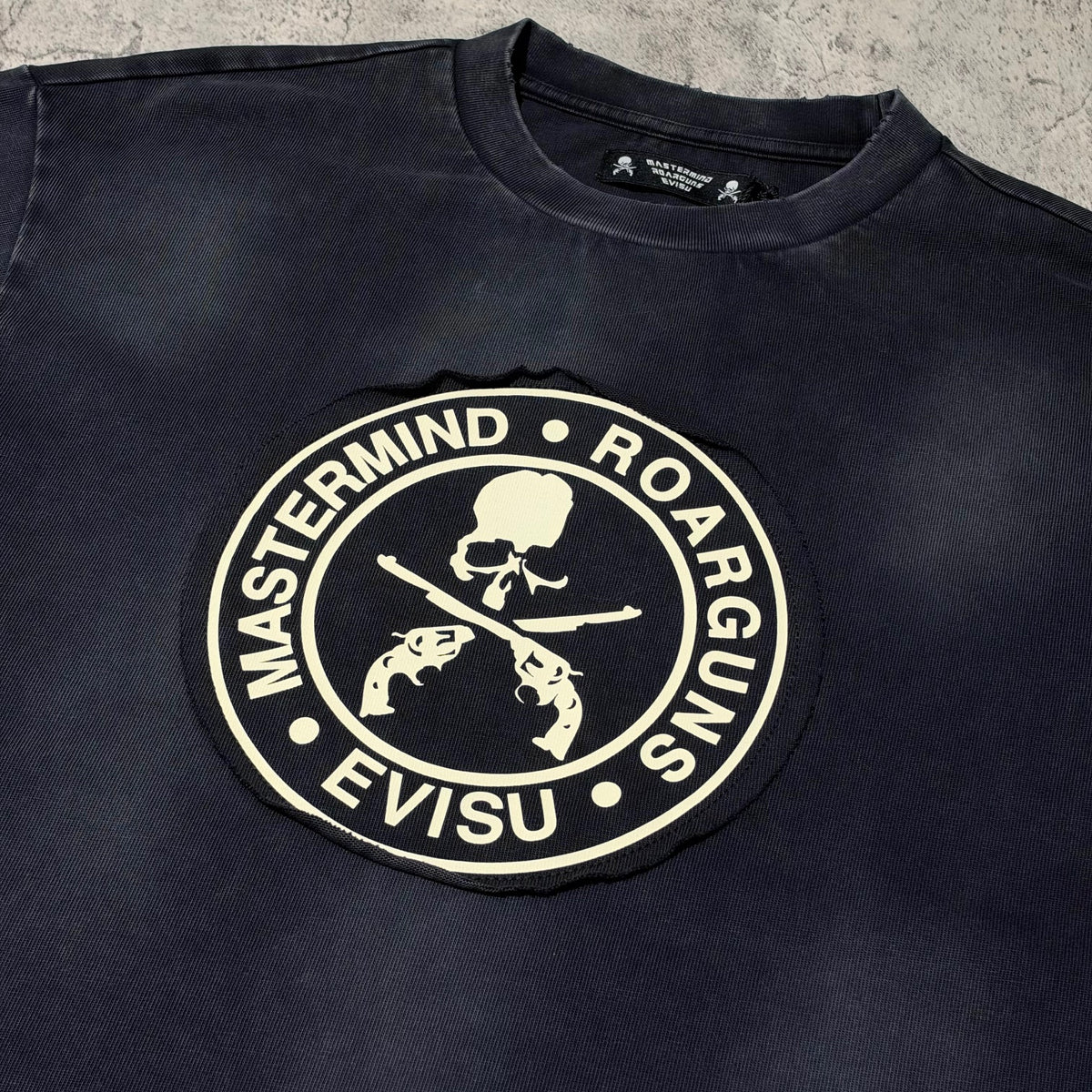 Evisu x Mastermind Japan x Roarguns Tee featuring a skull and crossbones logo on a dark background.