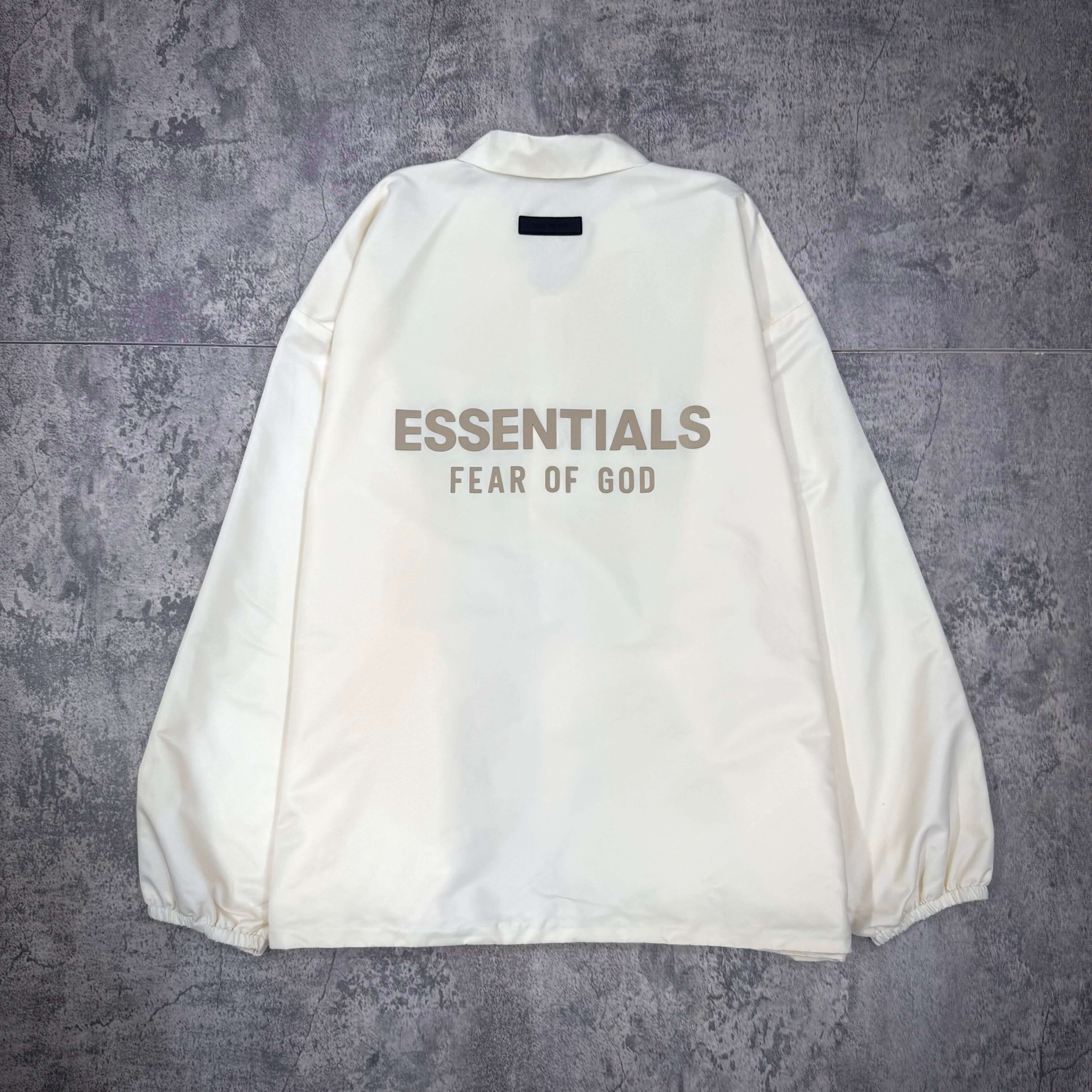 現貨 FOG Essentials Coaches Jacket FW23 - Cloud Dancer 背面視角,展示淺色外套及其文字設計。