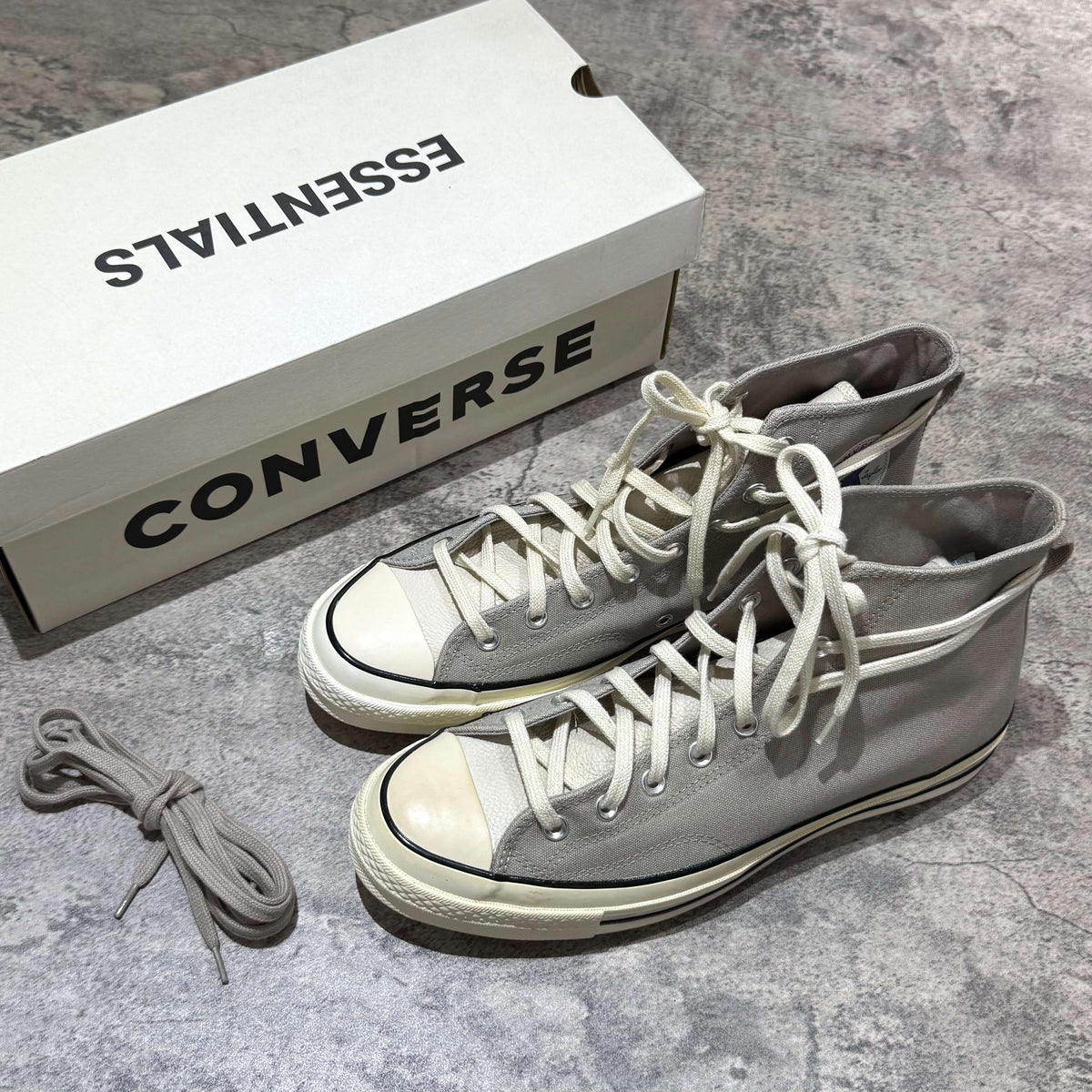 Fear Of God Essentials x Converse Chuck 70s Hi - White / Grey sneakers next to the box on a textured surface.