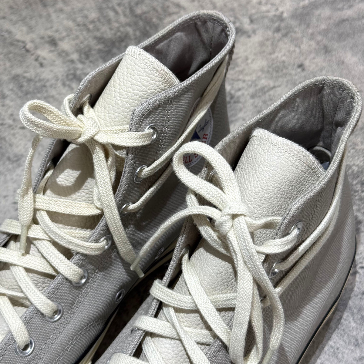 Close-up view of Fear Of God Essentials x Converse Chuck 70s Hi in white and grey, showcasing laces and texture.