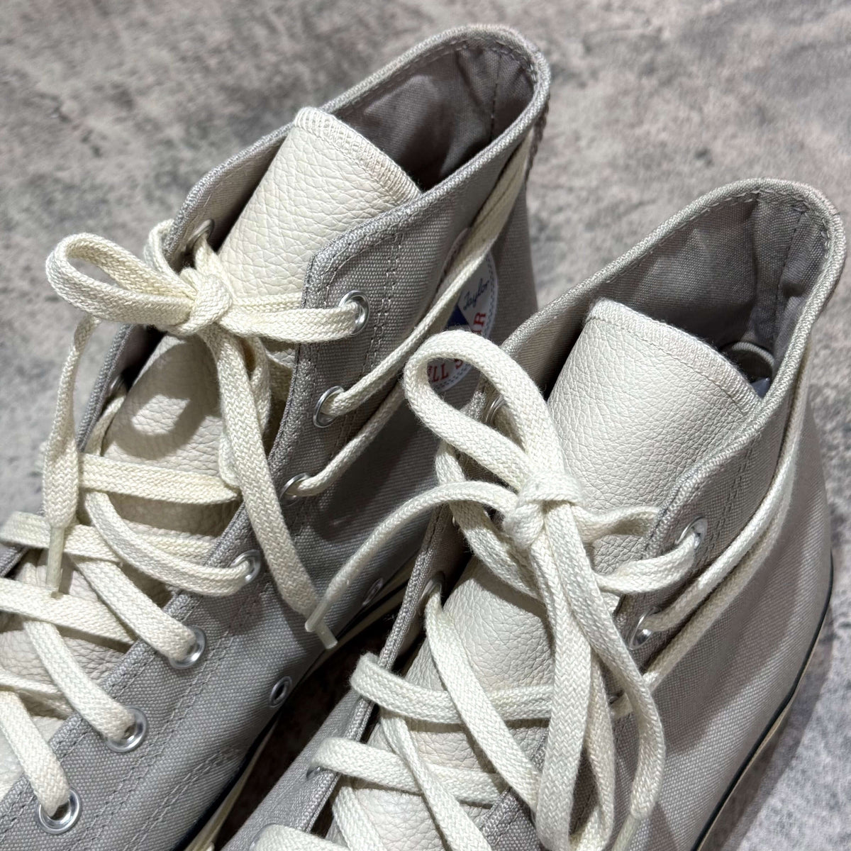 Close-up view of Fear Of God Essentials x Converse Chuck 70s Hi in white and grey, showcasing laces and texture.