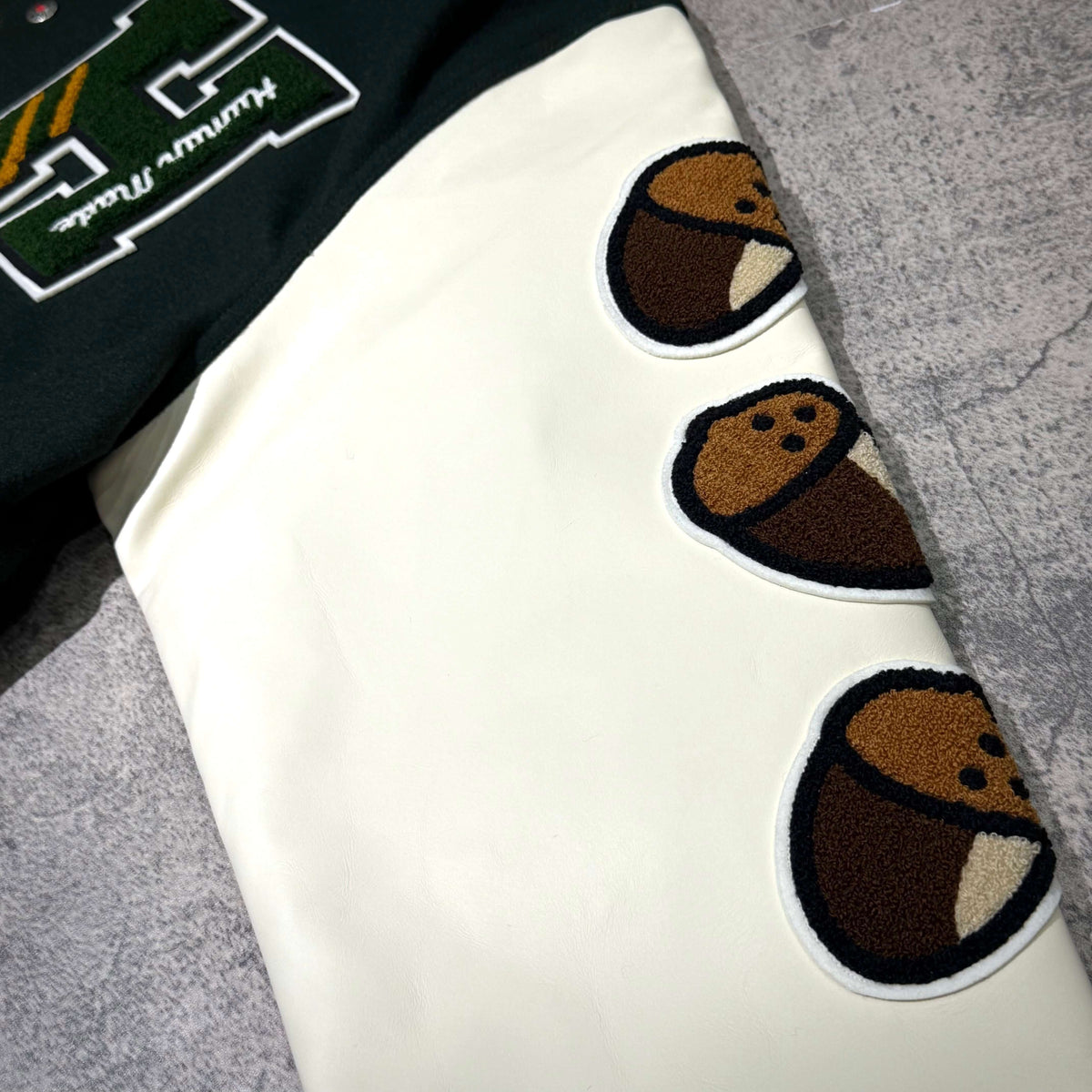 Detail of HUMAN HOPE Varsity Jacket HUMAN MADE x j-hope of BTS showing cup noodle graphic and embroidered patches.