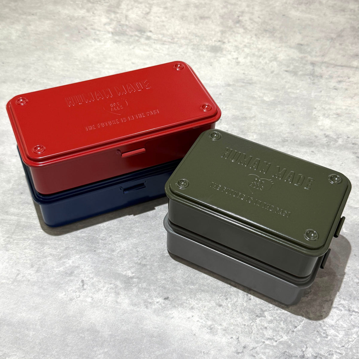 Human Made Steel Tool Box in red, navy, and green stacked on a gray surface.