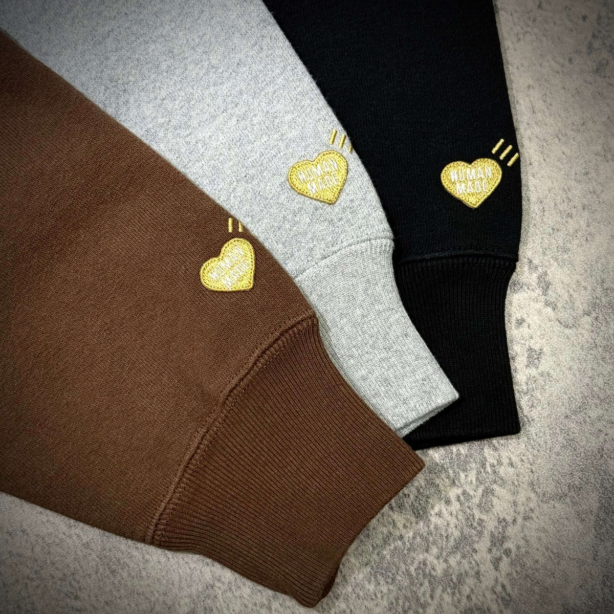 Human Made Tokyo Exclusive Lion Heavyweight Hoodie color options in brown, grey, and black with heart logo details.