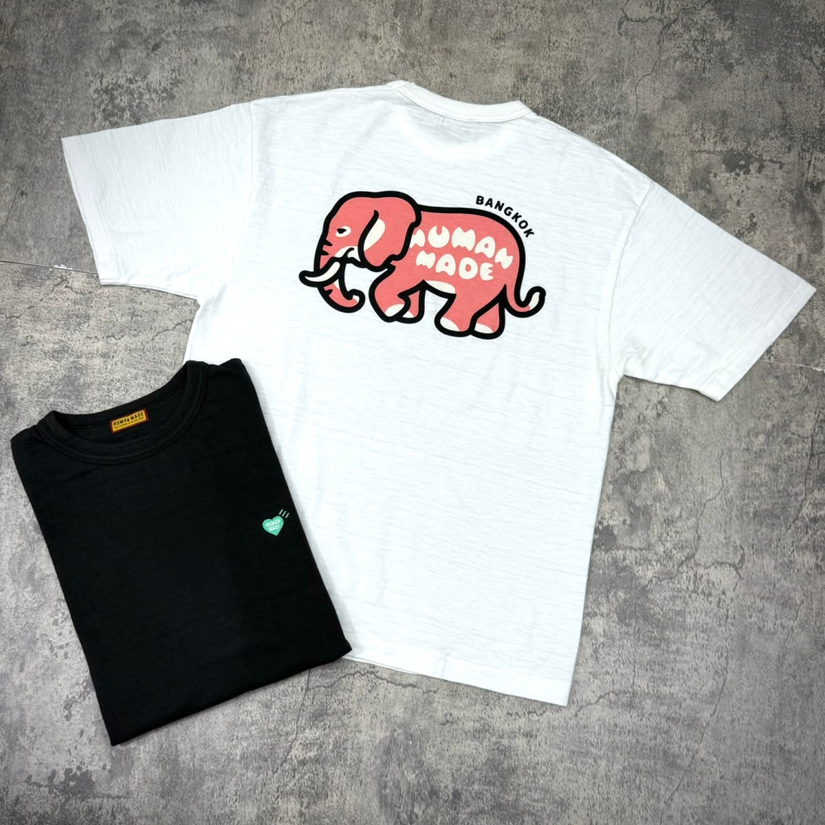 Human Made Bangkok Exclusive Elephant Back Logo Tee displayed with a black tee underneath, showcasing unique designs.