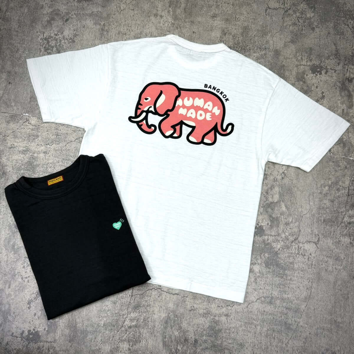 Human Made Bangkok Exclusive Elephant Back Logo Tee displayed with a black tee underneath, showcasing unique designs.