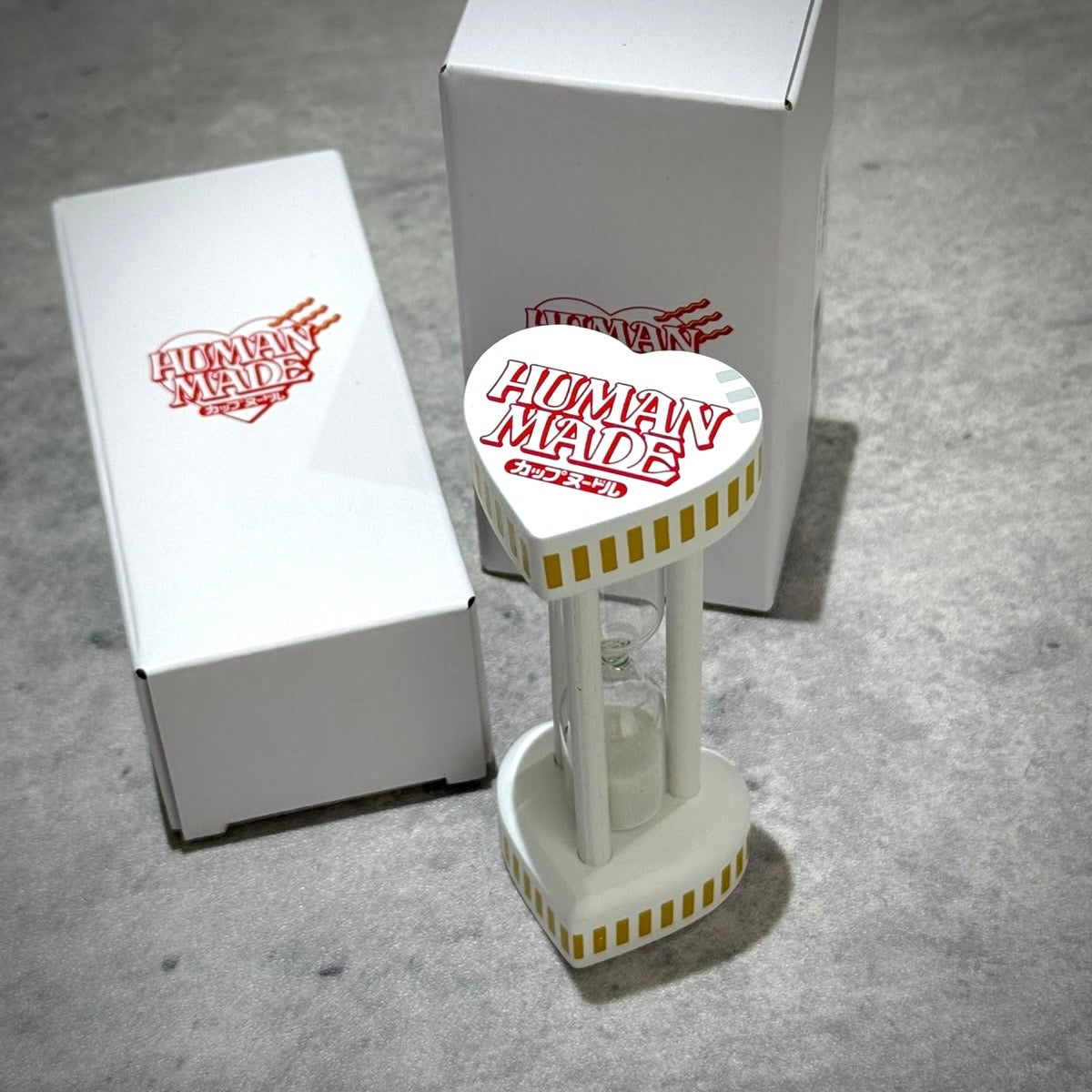 Human Made Cup Noodle 3 Minutes Hourglass alongside its packaging on a gray surface.
