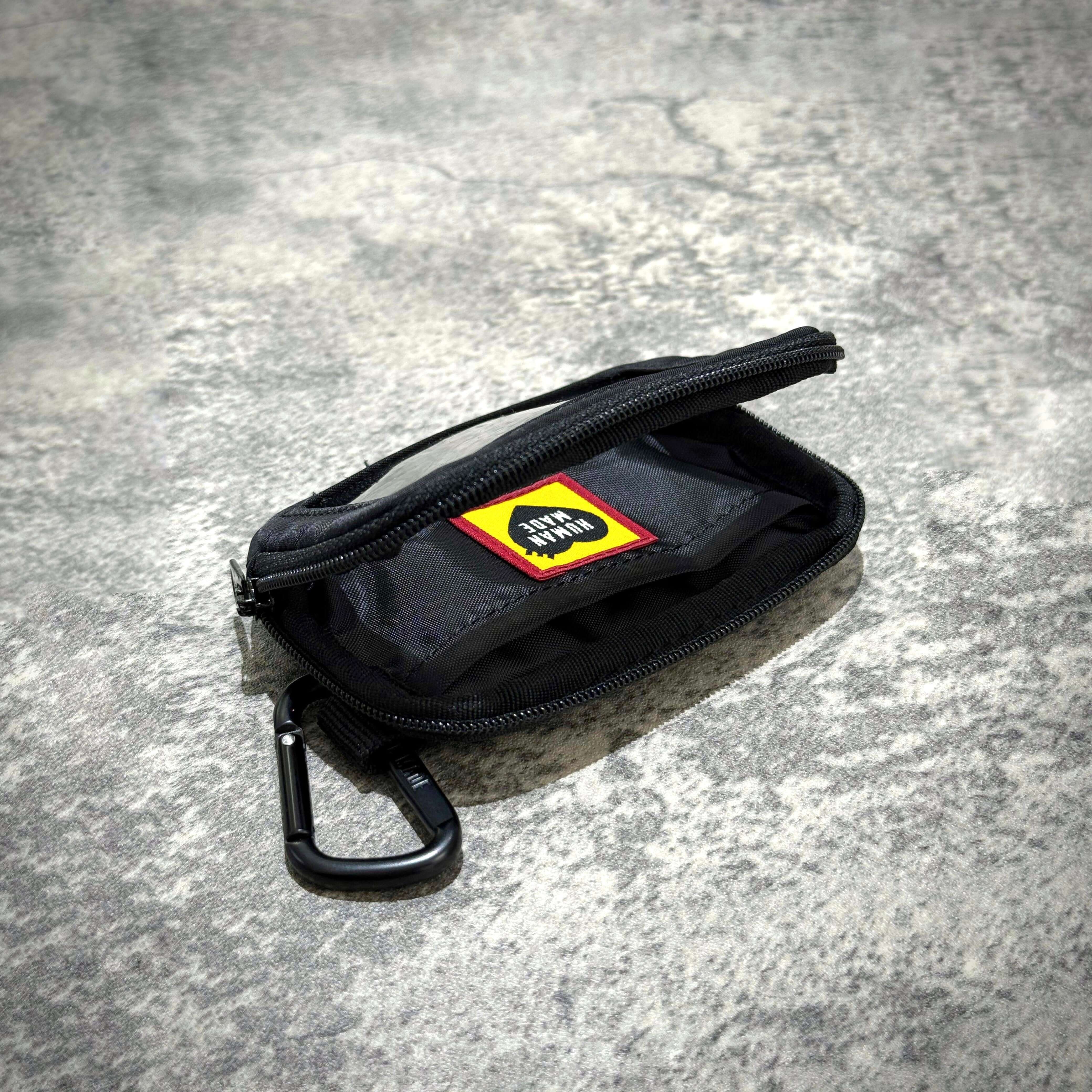 Human Made Military Card Case with zipper and carabiner on textured surface.