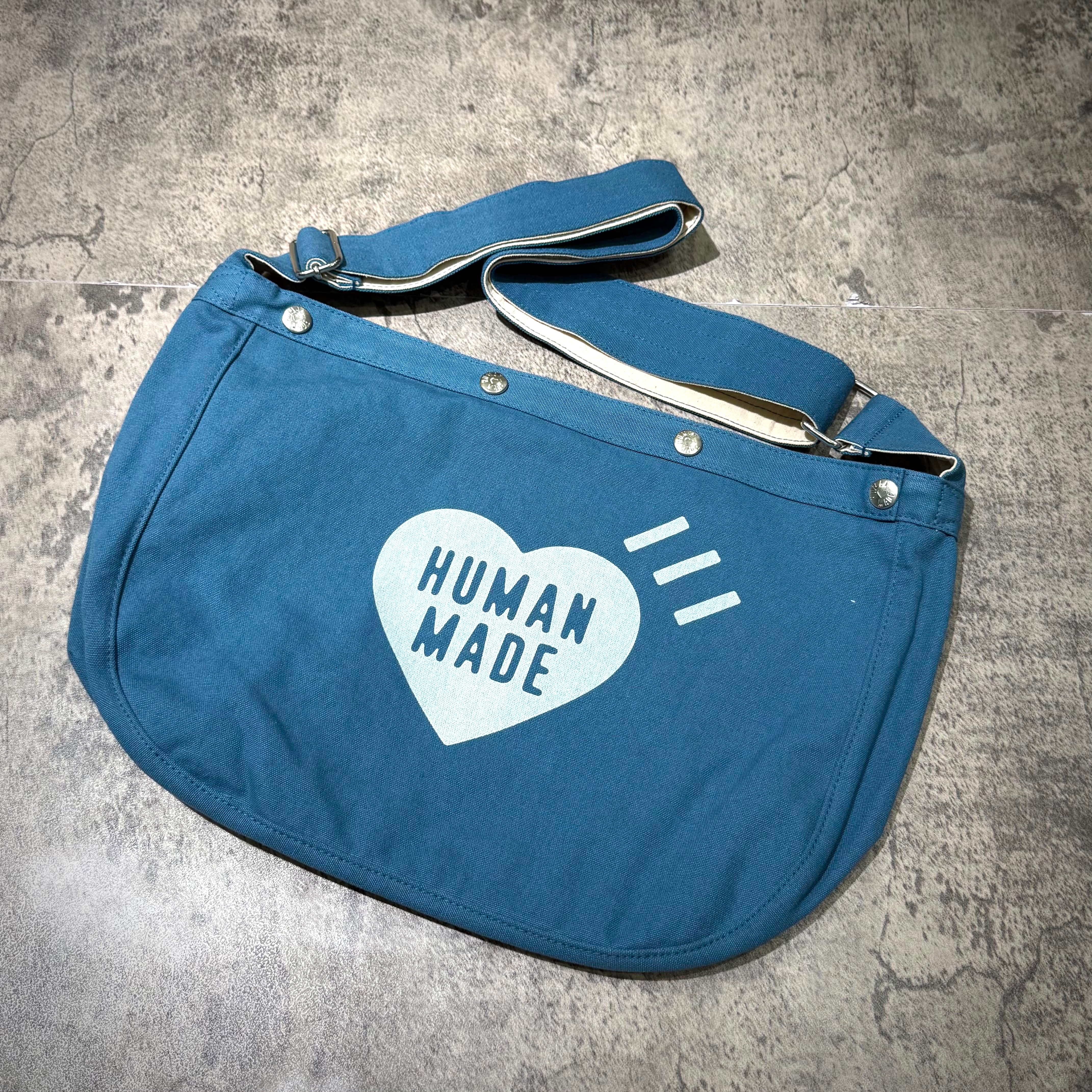 Human Made Paper Boy Bag featuring a blue canvas design with 'HUMAN MADE' logo and adjustable strap.