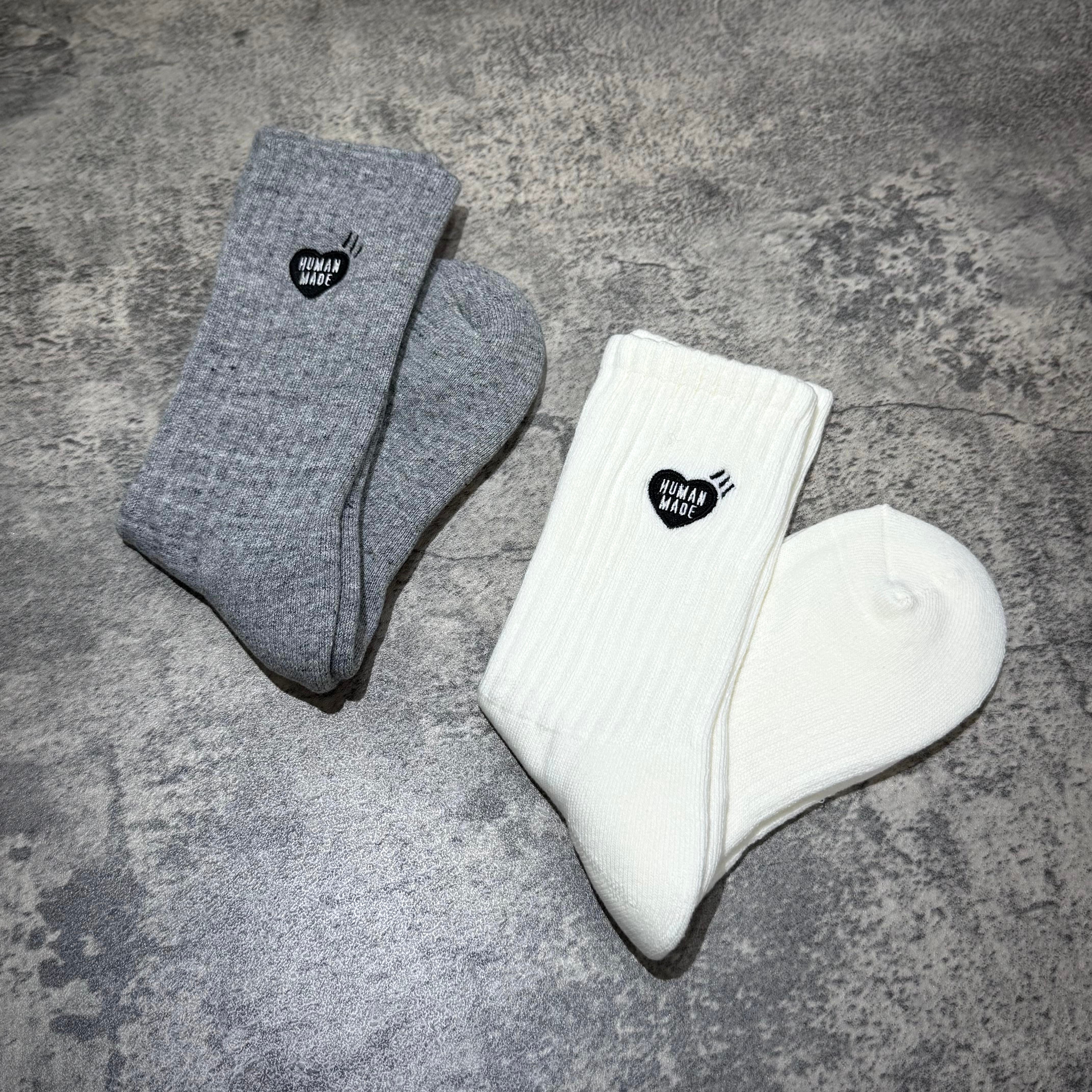 Human Made Pile Socks in gray and white laid on a textured surface, showcasing their unique design and branding.
