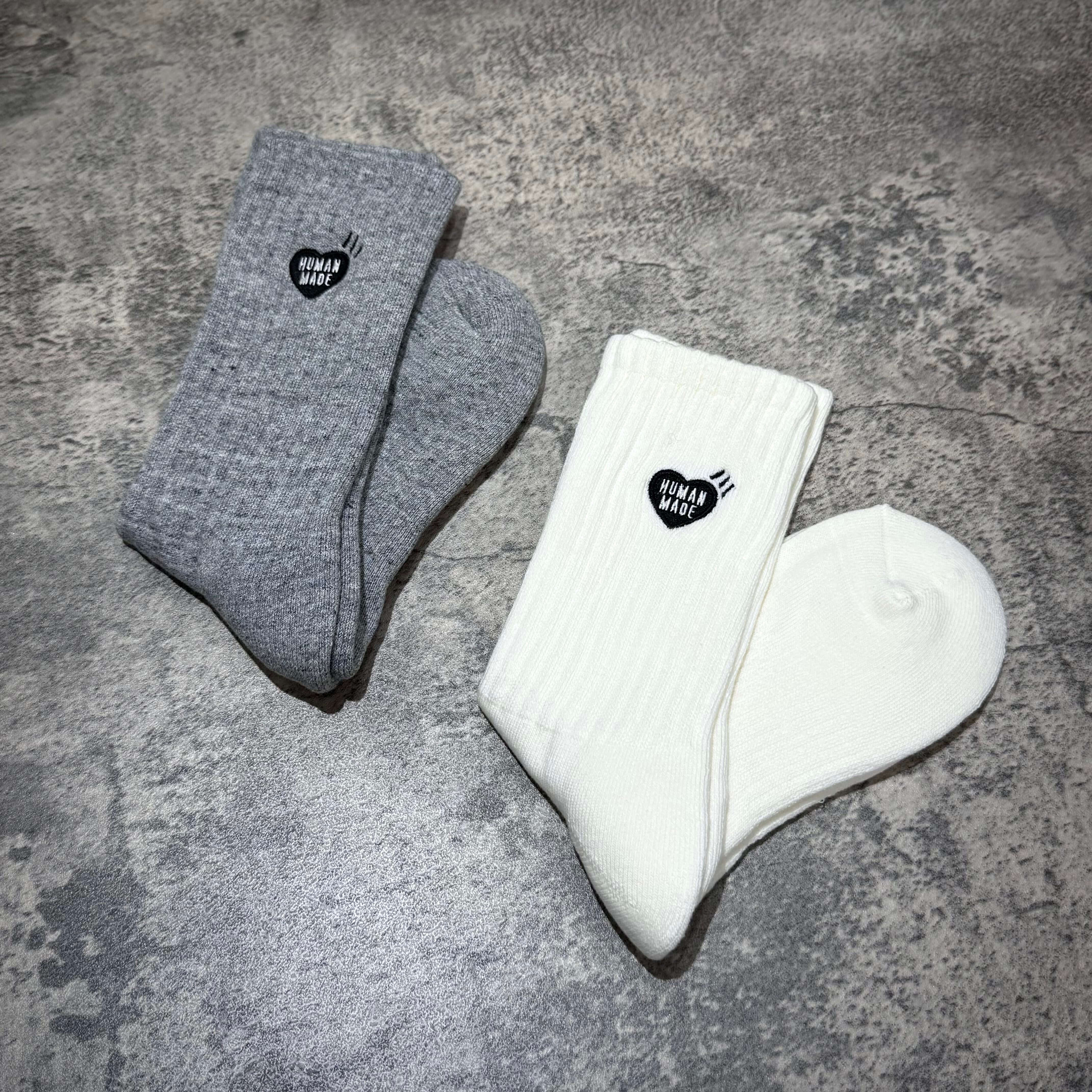 Human Made Pile Socks in gray and white laid on a textured surface, showcasing their unique design and branding.