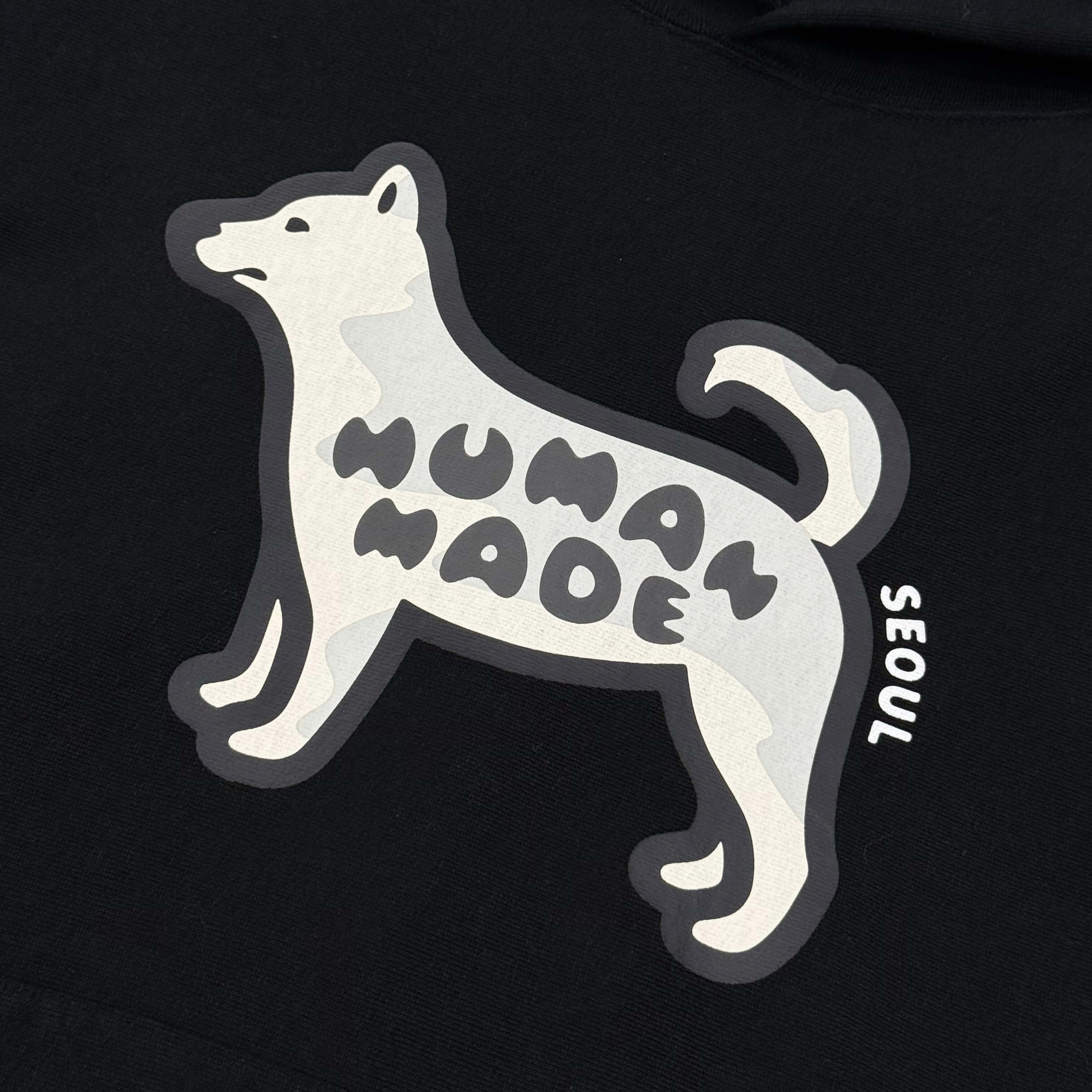 Graphic of a dog with 'HUMAN MADE' and 'SEOUL' text on a black hoodie from Human Made Korea.