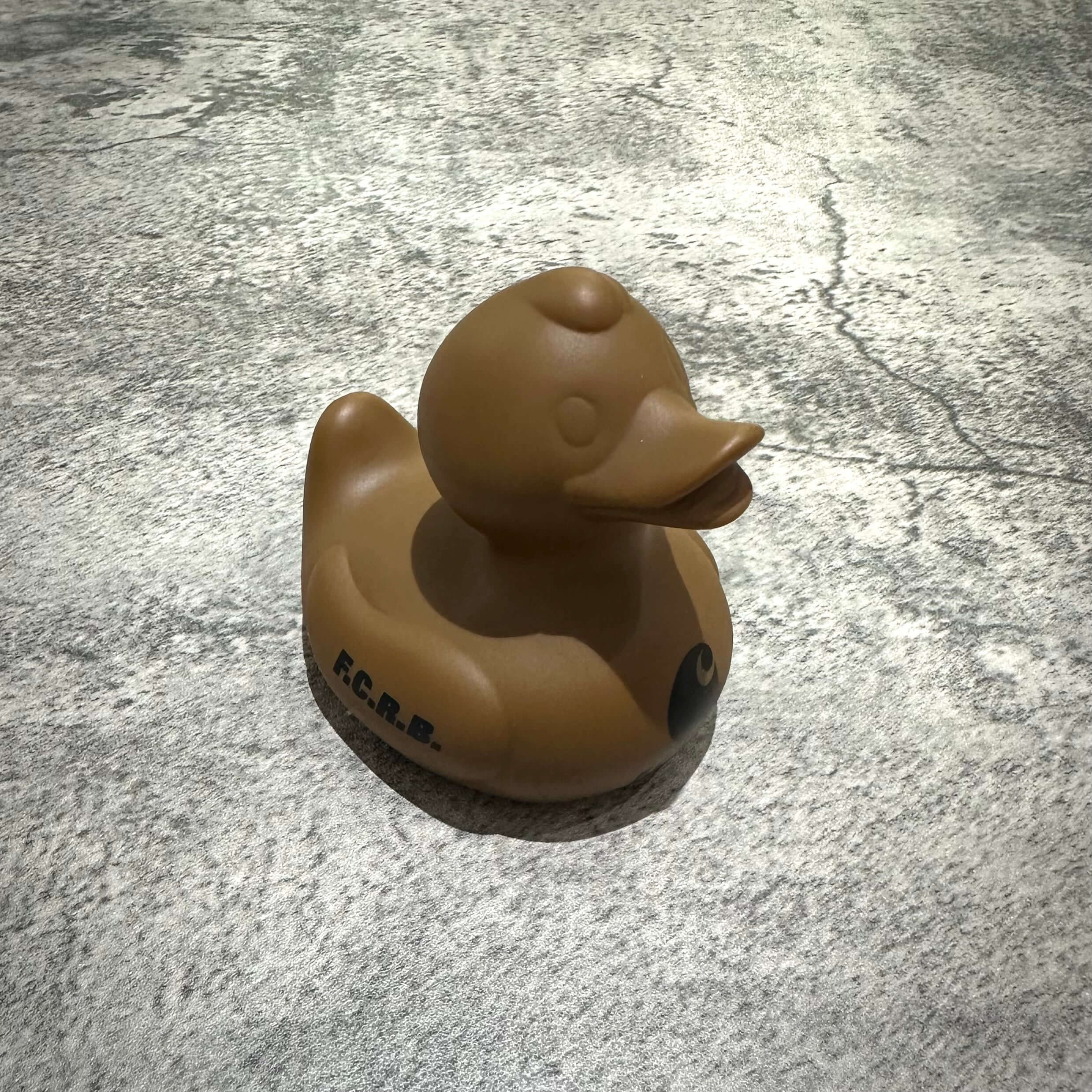 Carhartt WIP x FCRB Rubber Duck on a textured surface, showcasing its unique design and color.