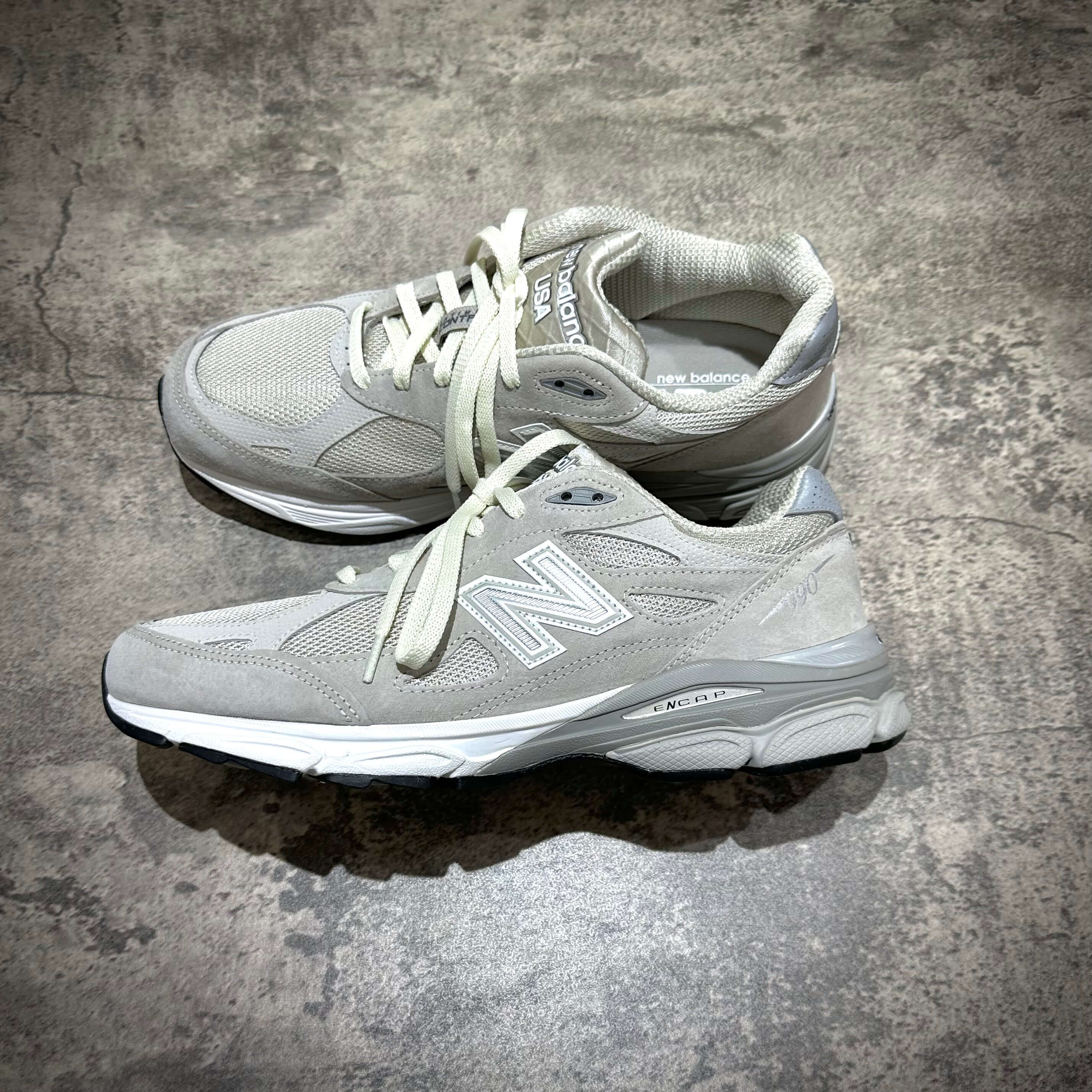 MiUSA Kith x New Balance 990v3 Hallow grey athletic shoes top view on textured surface.