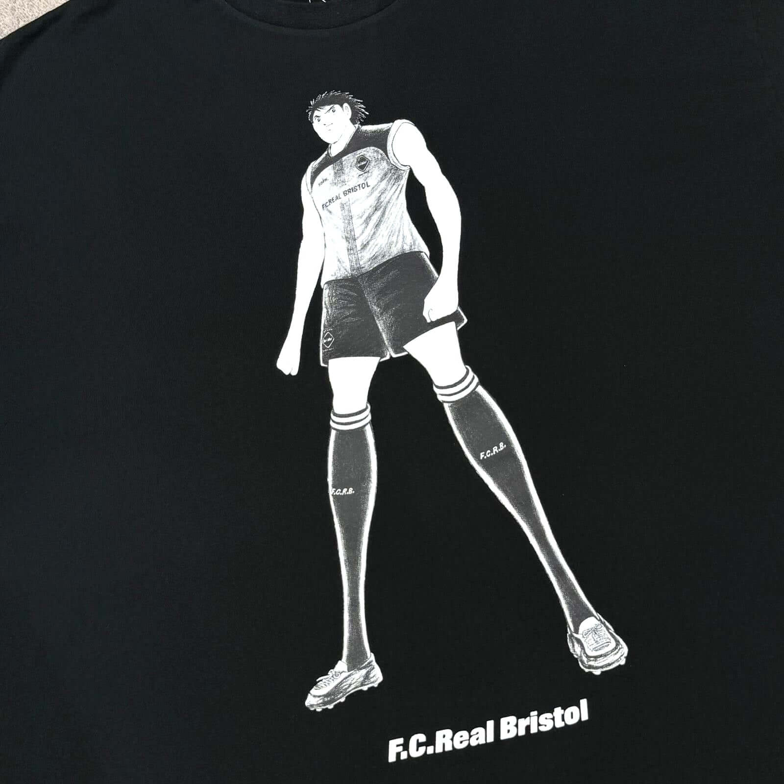 Kojiro Hyuga x FCRB On The Front Baggy Tee featuring F.C. Real Bristol graphic design on a black shirt.