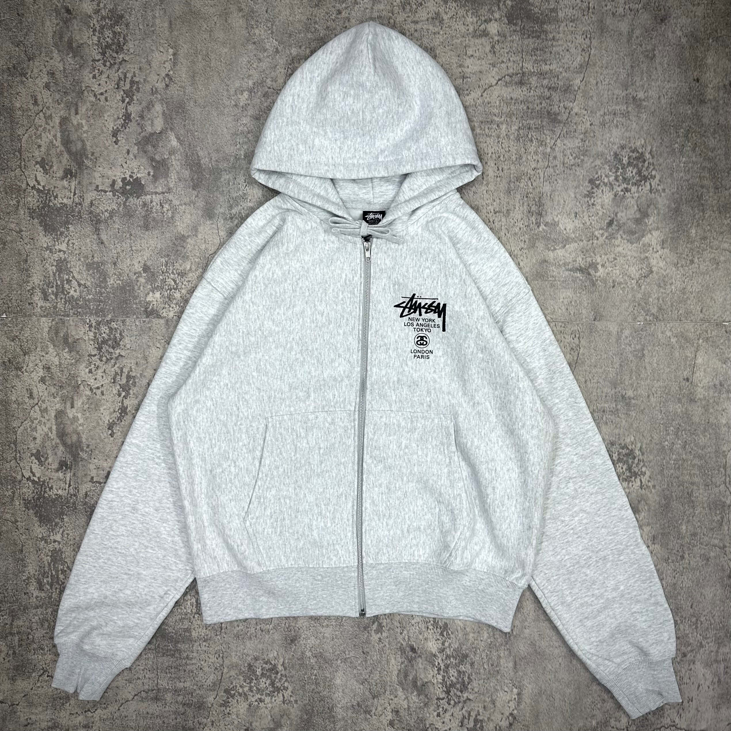 現貨 Stussy World Tour Zip Hoodie - Navy / Black / Grey,顏色為淺灰色,附帶連帽和拉鍊設計。