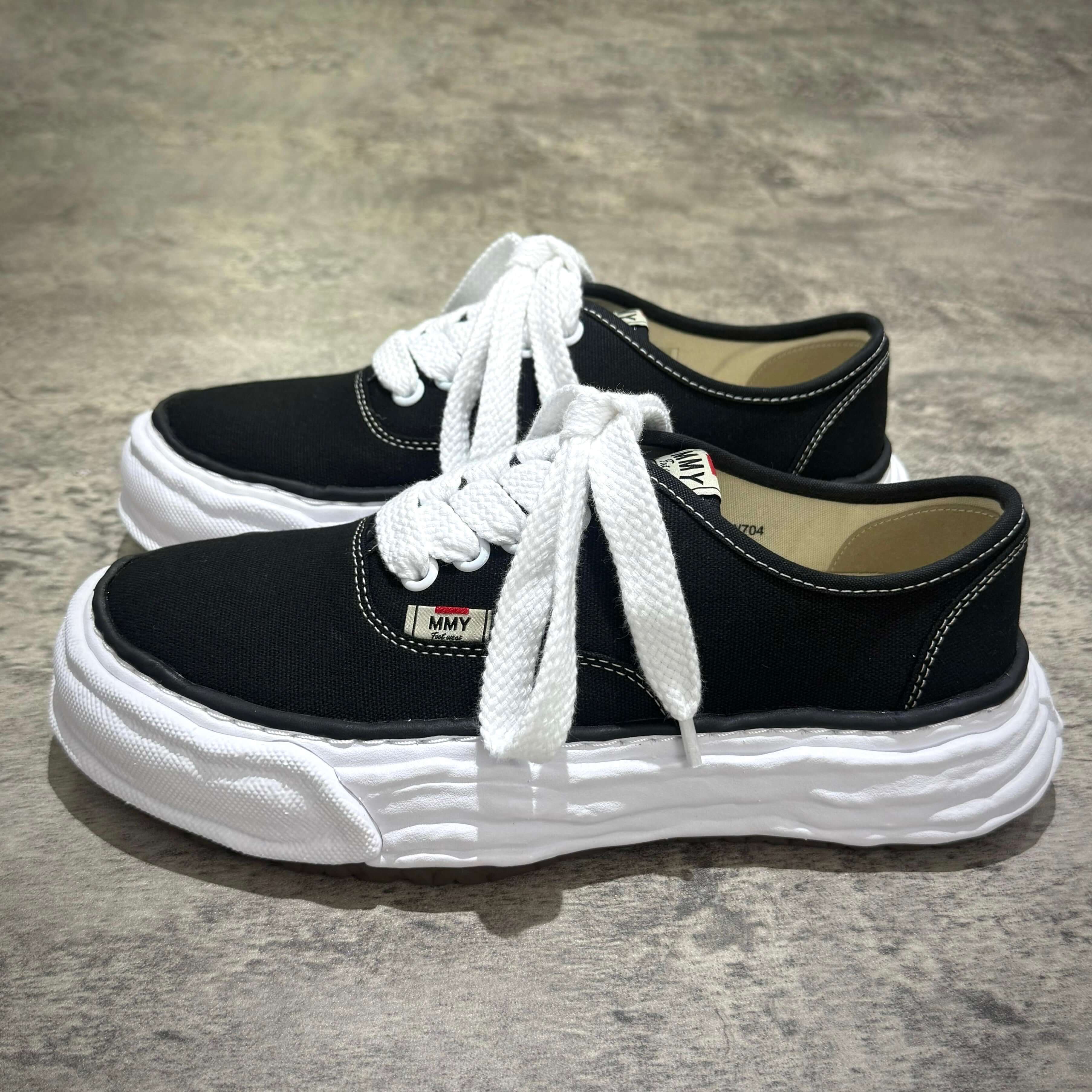 MMY Baker26 Canvas Low - Black sneakers with oversized design and white laces on a textured background.