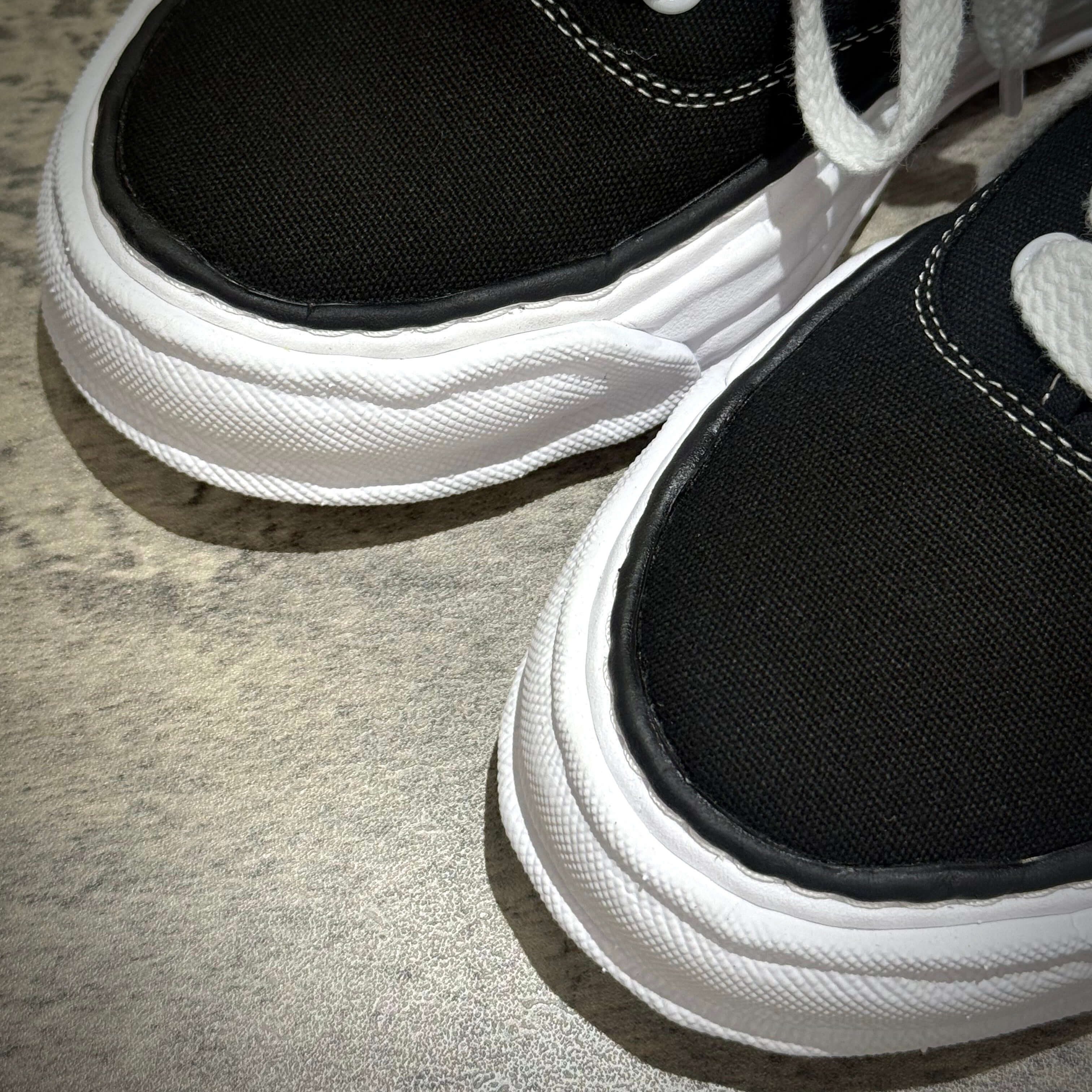 Close-up of MMY Baker26 Canvas Low - Black sneakers showing black canvas upper and white sole details.