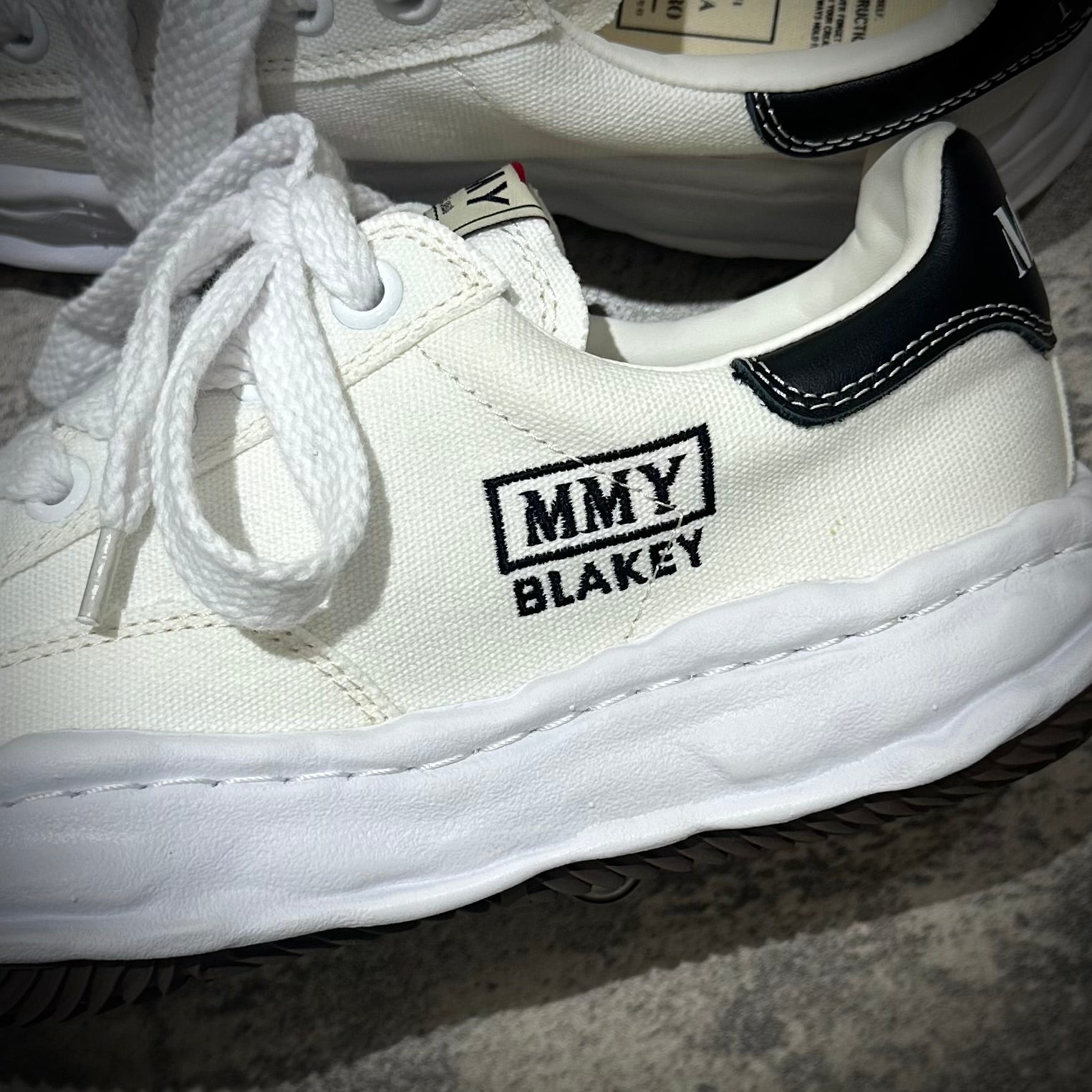 Close-up of MMY BLAKEY sneakers in white canvas with black accents and textured sole.