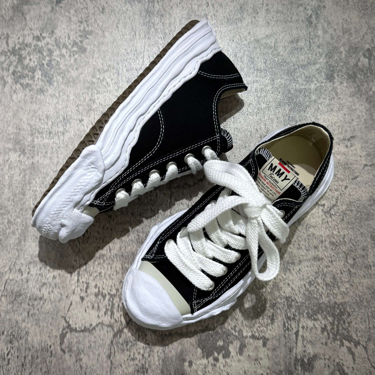 MMY HANK OG Canvas - Black high-top sneakers with white laces and stitching on a gray surface.