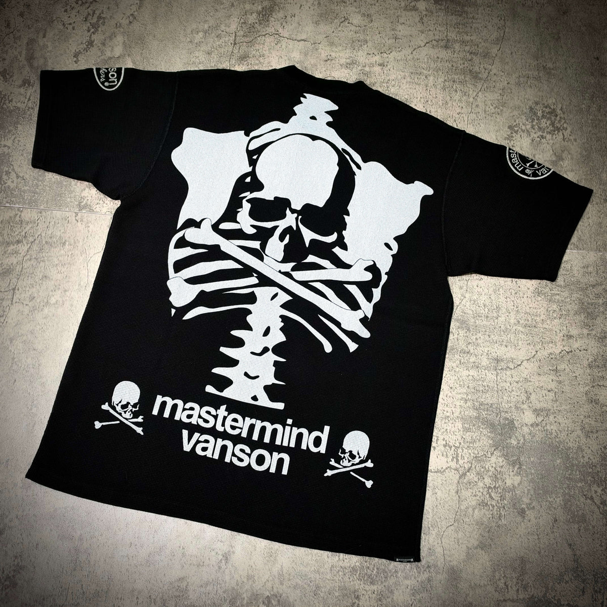 Mastermind World x Vanson Regular Fit Tee featuring skull and crossbones design on black background.